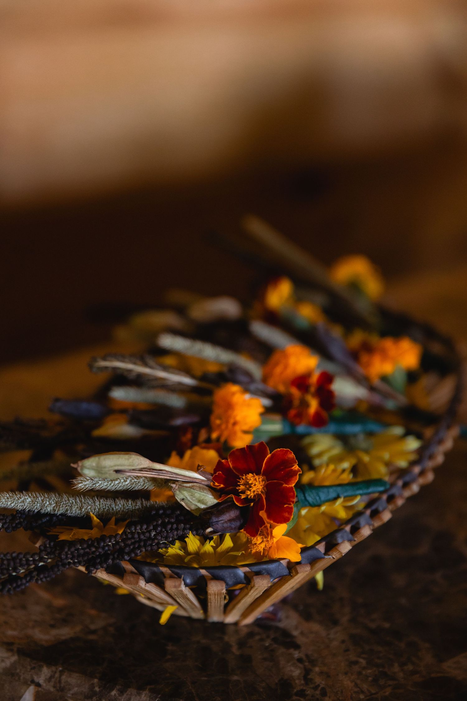 Colorful dried flowers and feathers arranged artistically on a rustic wooden surface in moody lighting.