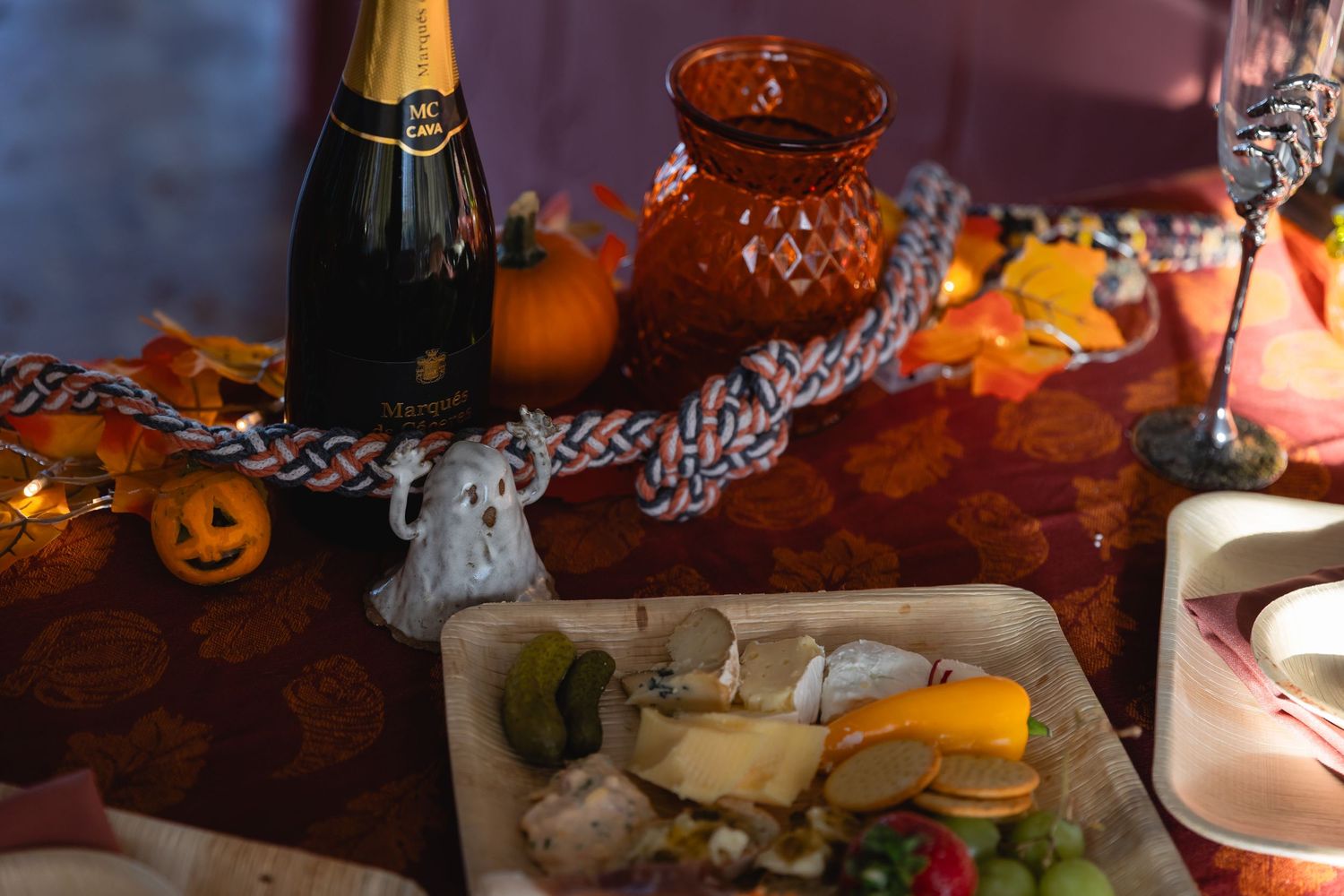 Halloween party table setting with champagne, decorative pumpkins, ghost lights and sandwich platter.