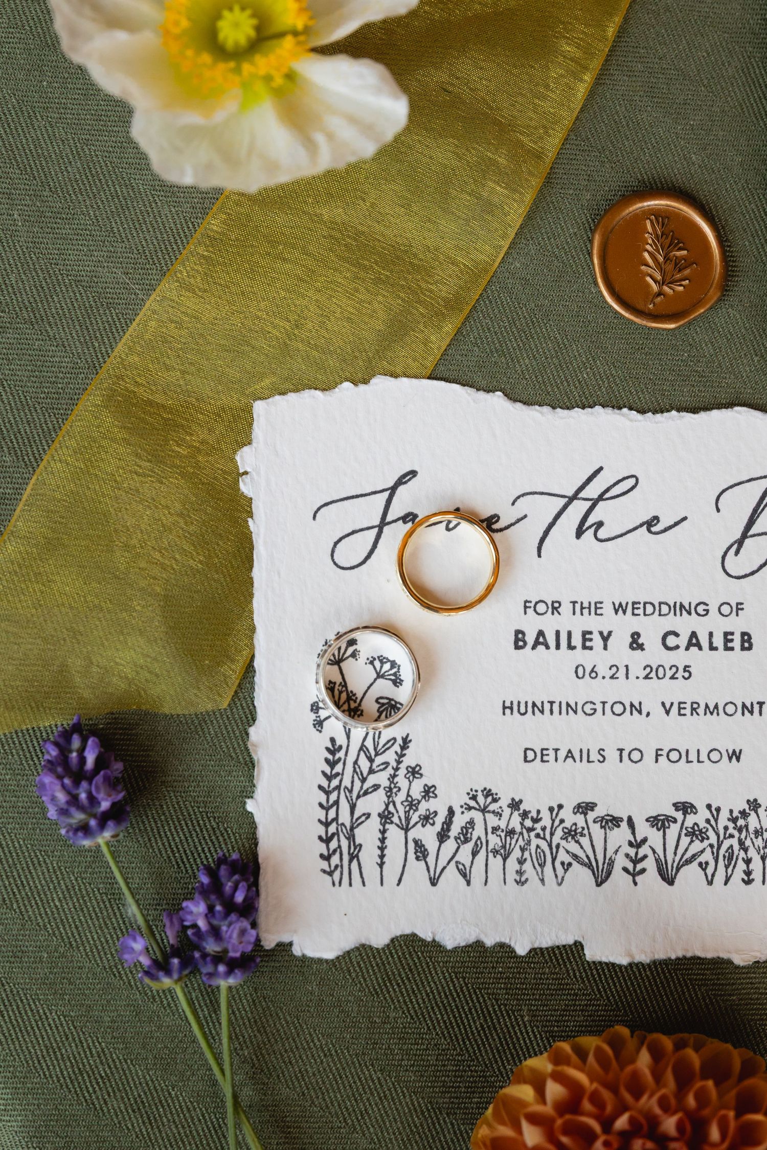 Wedding invitation details laid on green fabric with yellow poppies and purple lavender flowers as decorative elements.