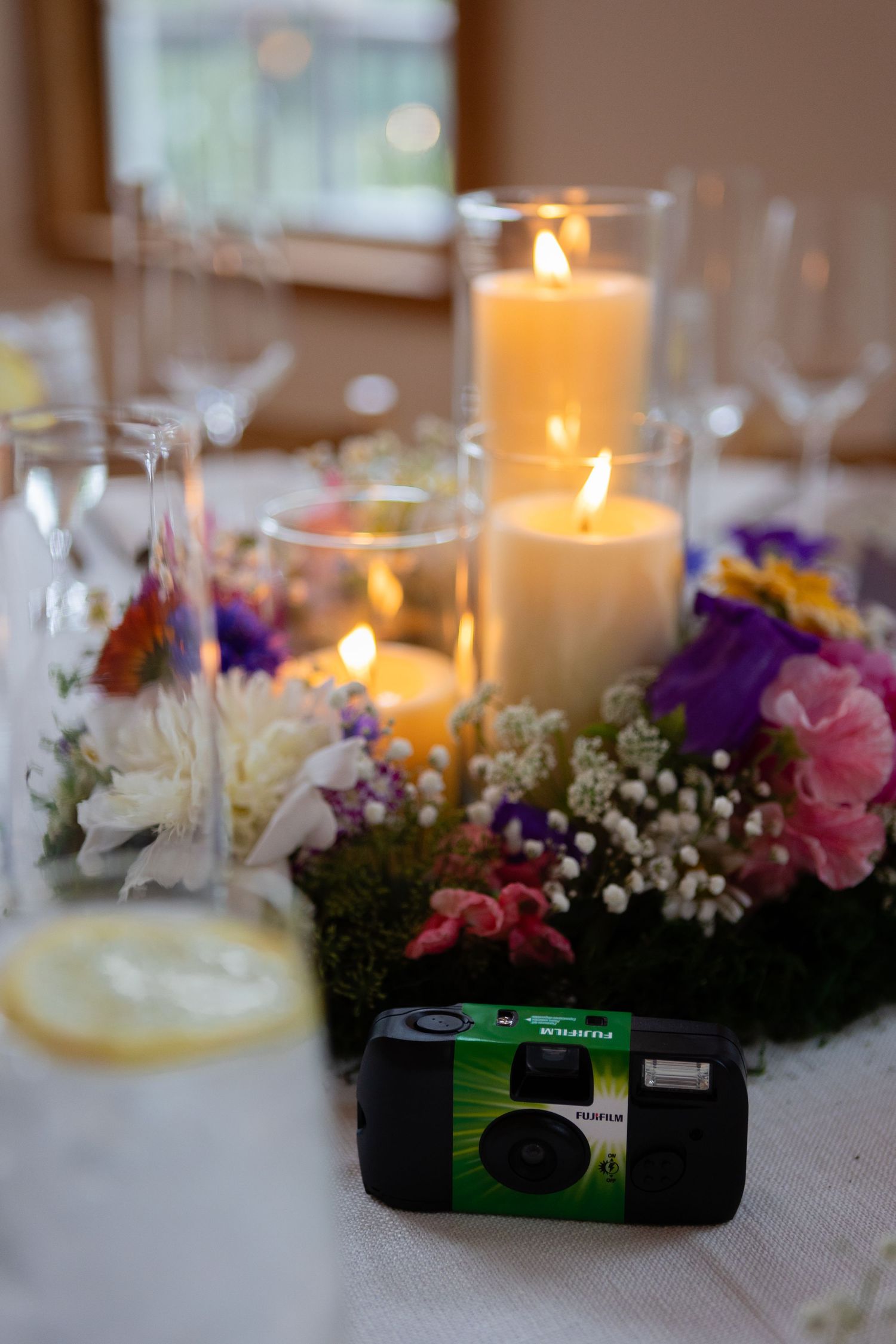 Wedding table centerpiece with white candles, colorful flowers, and a disposable camera.