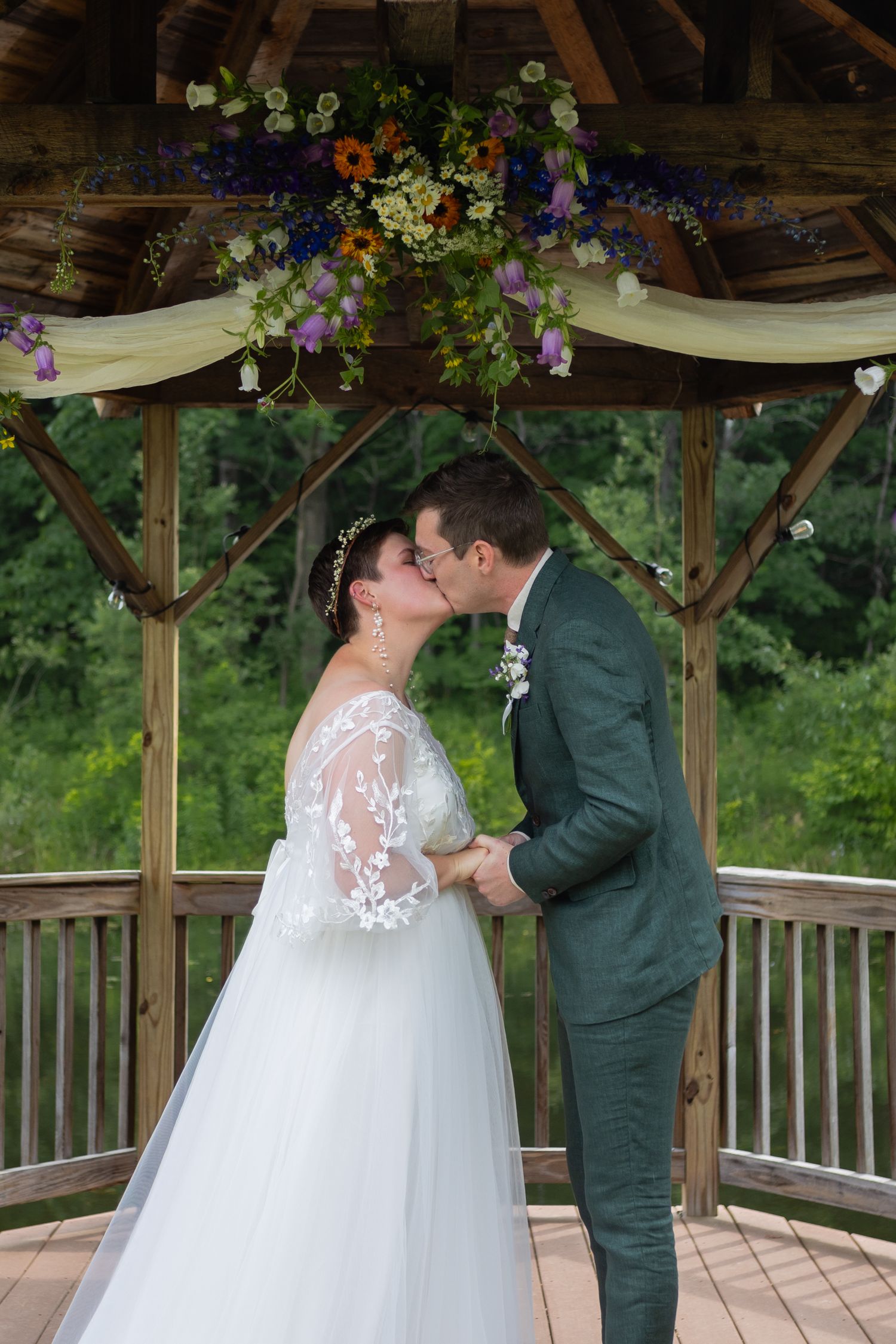 First kiss as newlyweds under a beautifully decorated gazebo with hanging flowers and draped fabric.