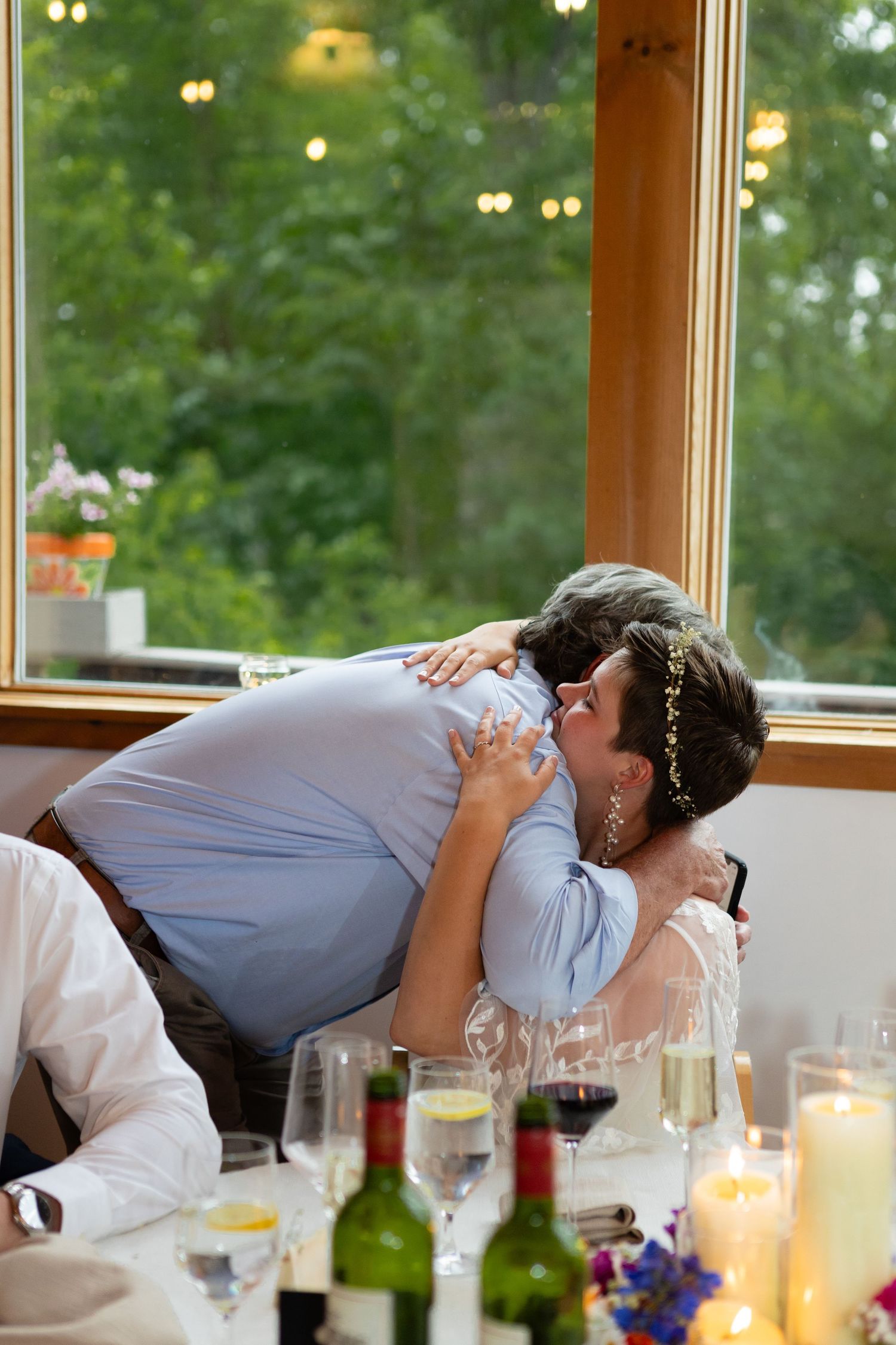 Intimate embrace during wedding reception dinner with wine glasses and candles on table.