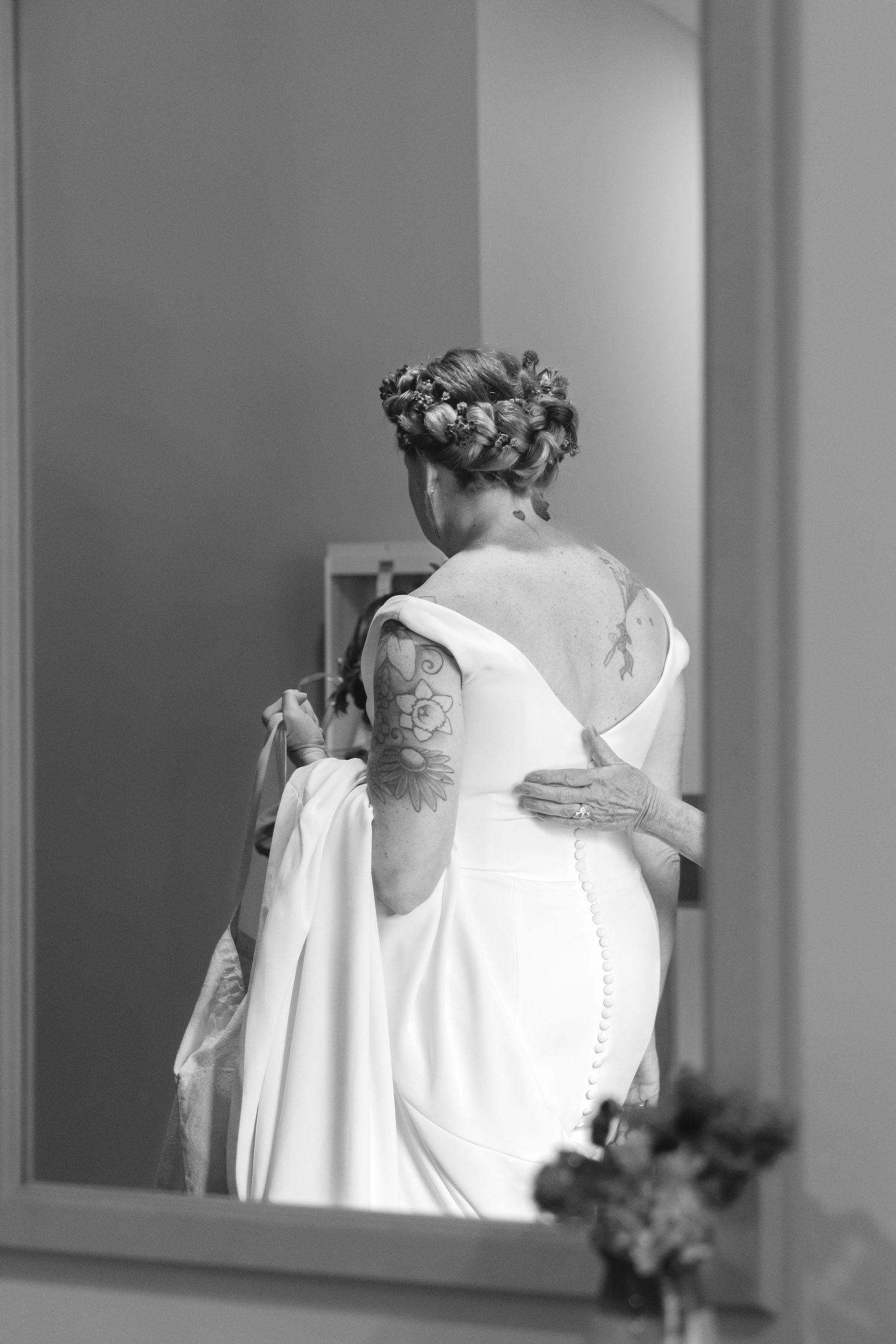 Black and white reflection of bride showing intricate back detail of wedding dress.
