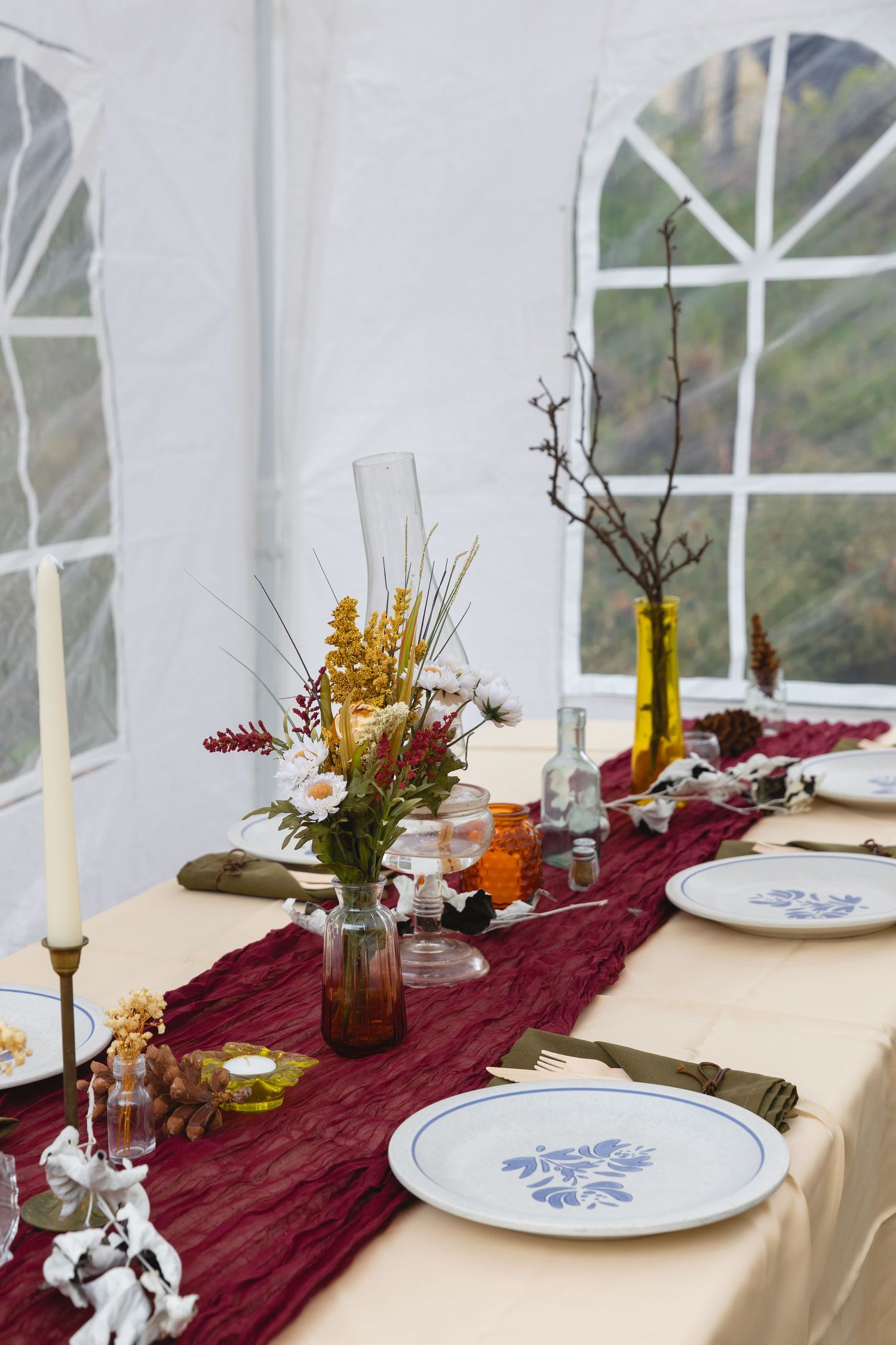 Elegant wedding table setting with burgundy runner, white plates, and wildflower centerpieces.