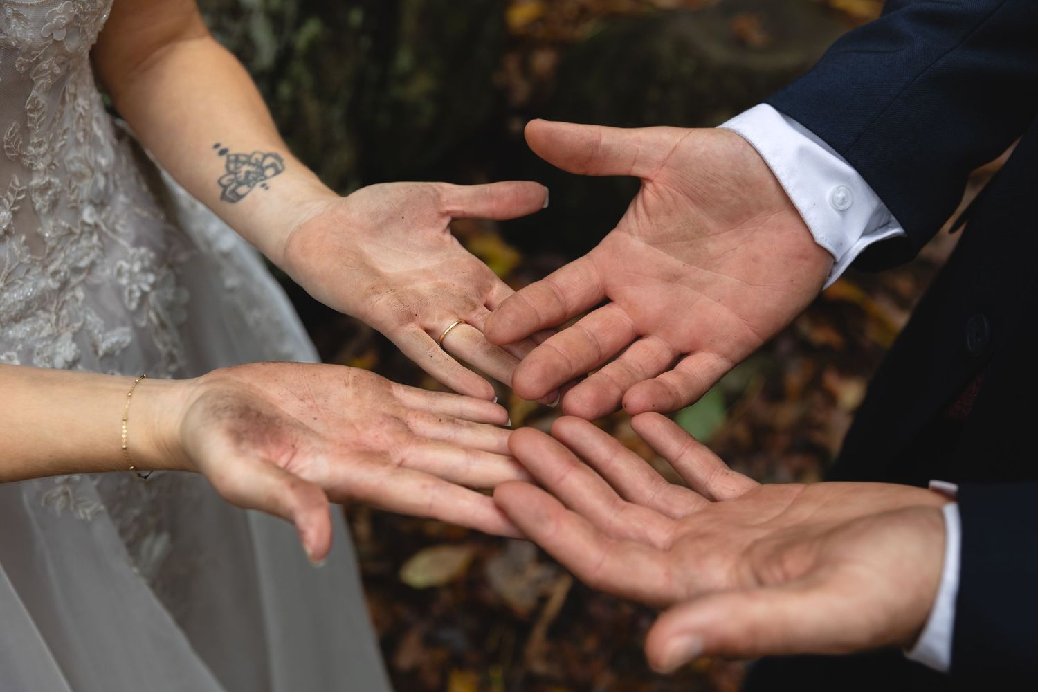 Close-up of hands joining together, showing wedding rings and delicate lace dress details.