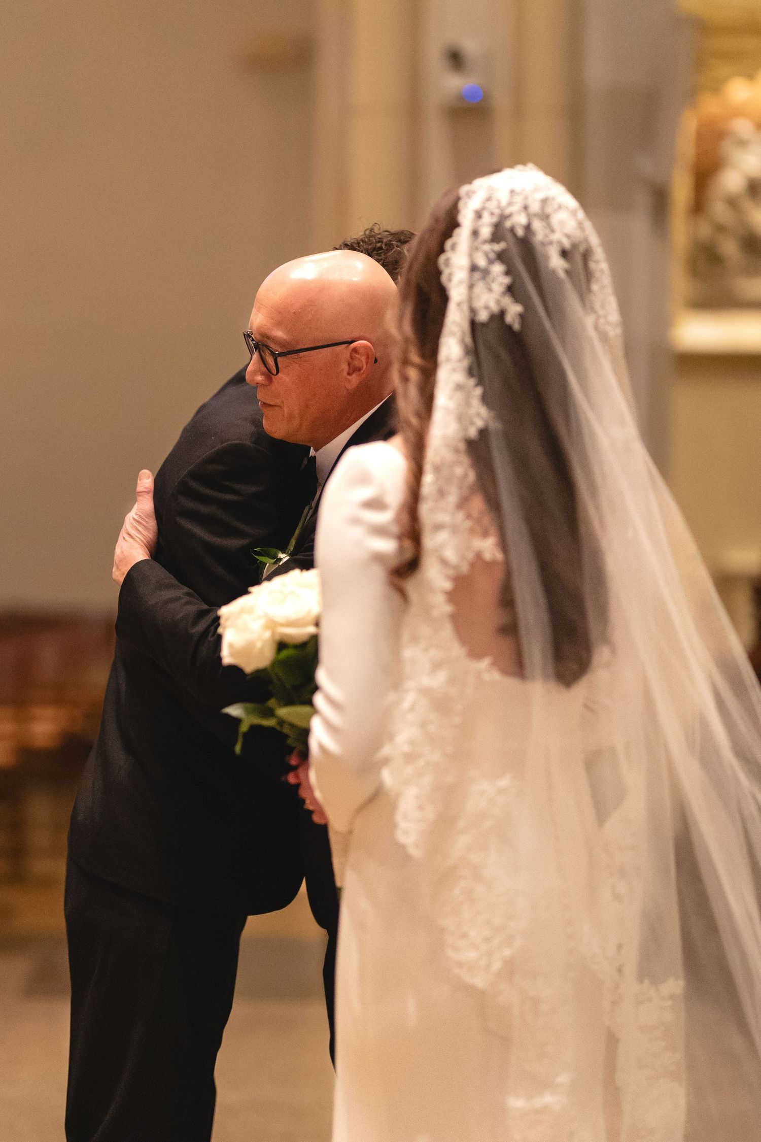 An emotional embrace during a wedding ceremony with the bride wearing a flowing white veil and lace dress.