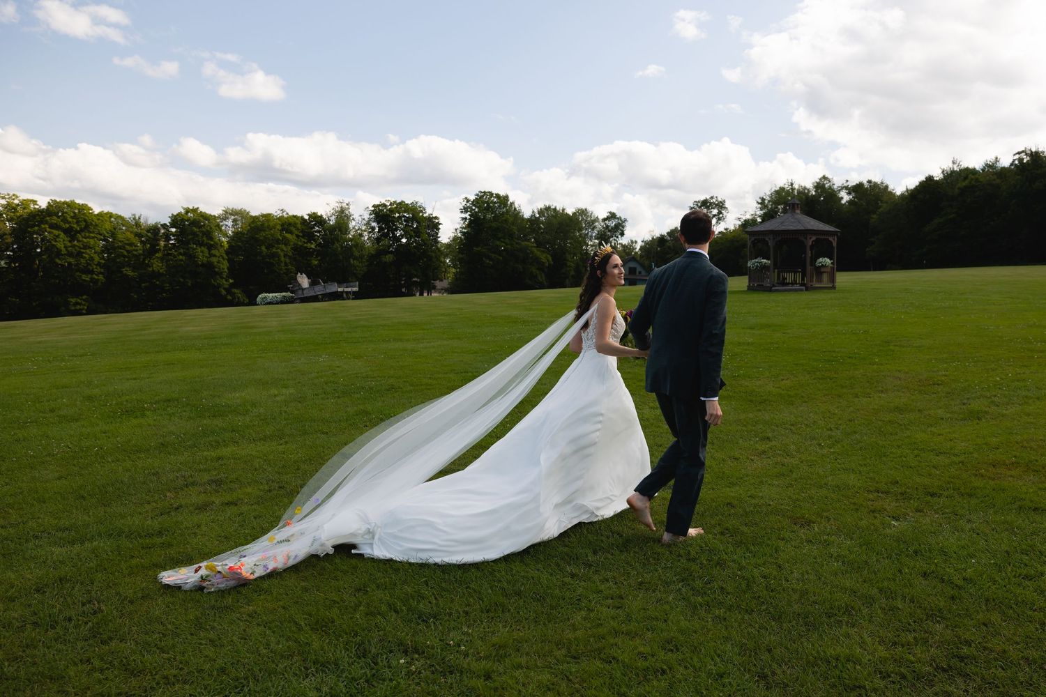 A couple walks across an open field with flowing wedding dress train.