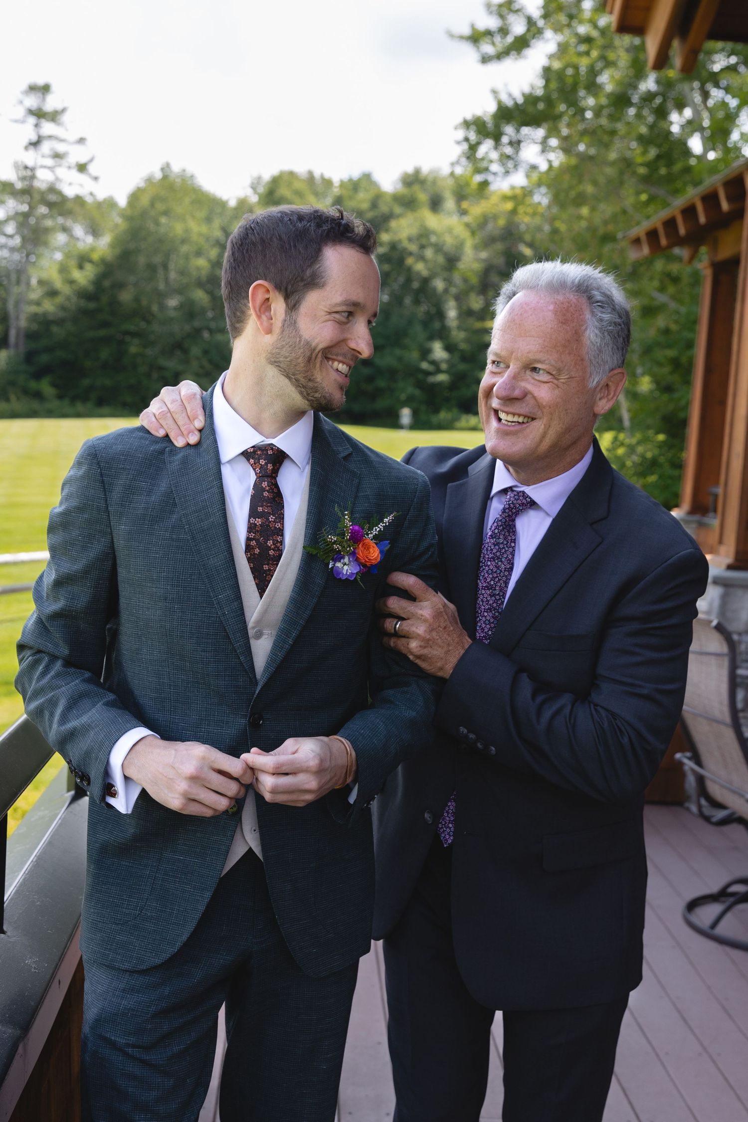 Two men in suits sharing a joyful moment on a deck with mountains in background.