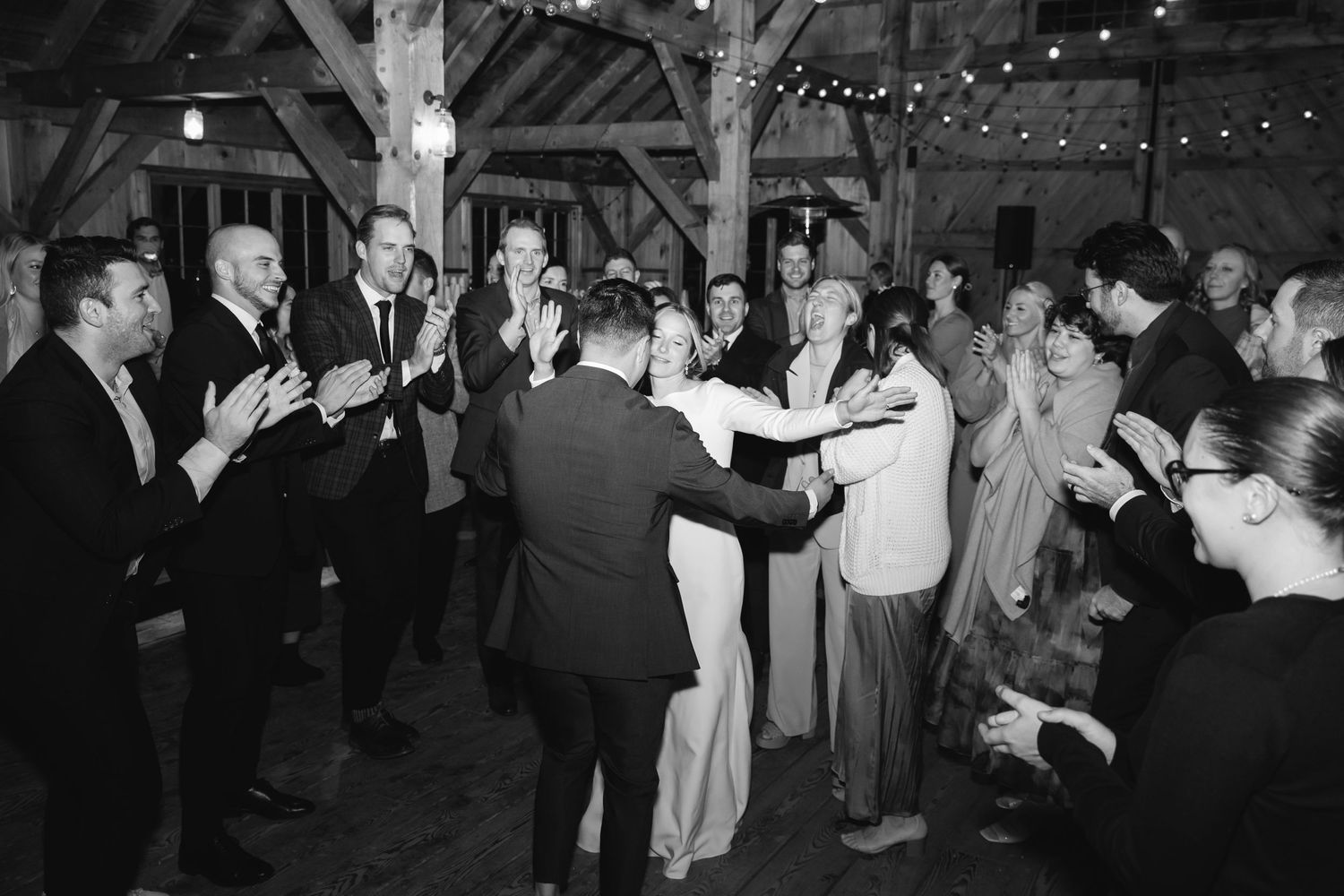 Vintage black and white photo of couples dancing at a rustic barn reception with string lights overhead.