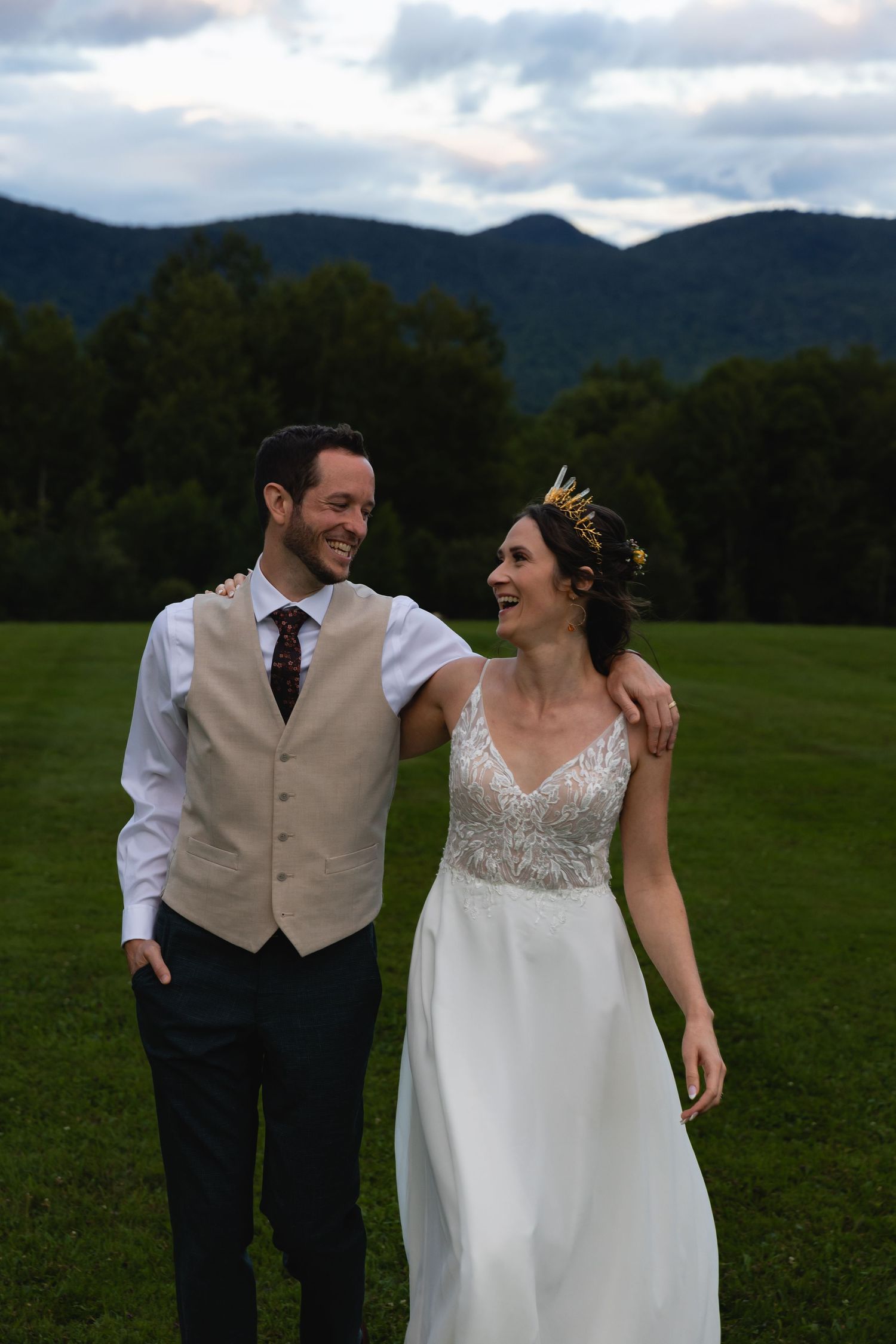 A joyful couple shares a laugh during their outdoor wedding photoshoot with mountains in the background.