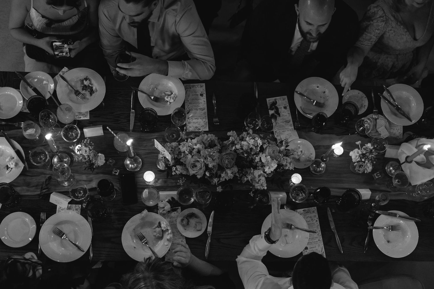 Overhead black and white view of people dining at a table with plates and candles during a restaurant meal.