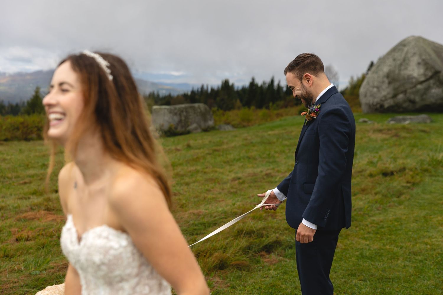 Playful wedding couple runs with their dog in a scenic mountain setting.