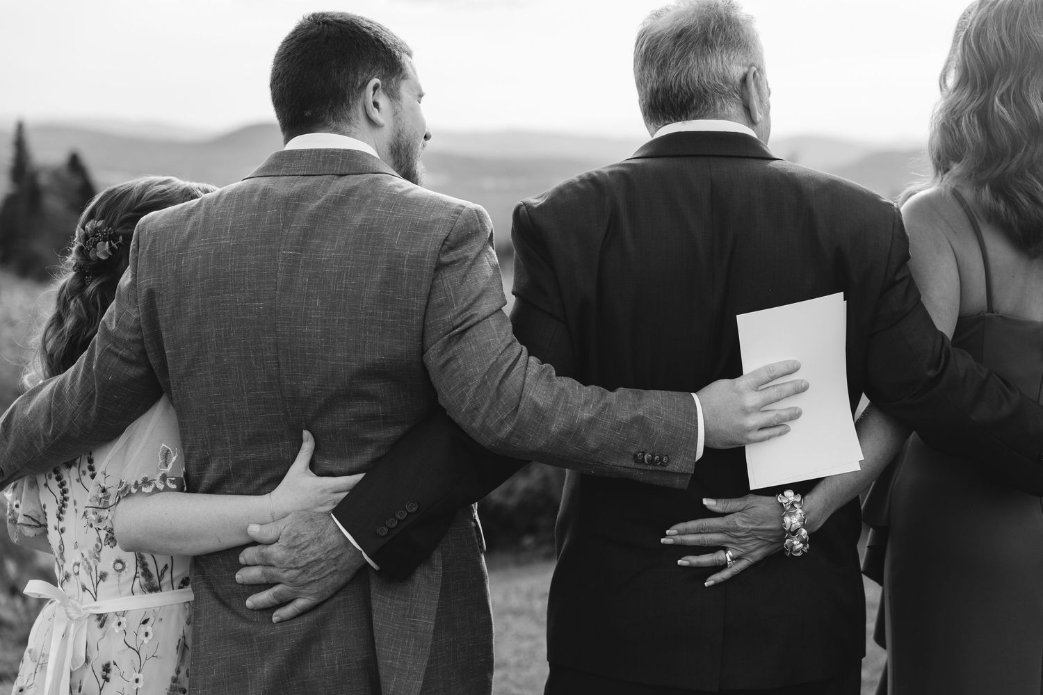 A row of people stand together with their arms around each other's backs in black and white.