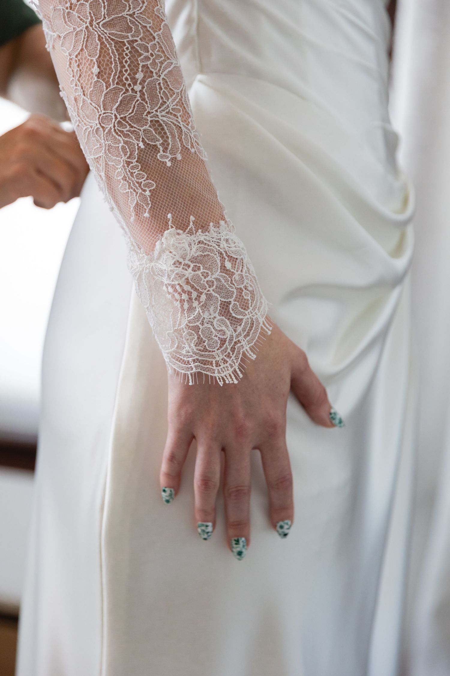Close-up of delicate white lace sleeve detail on a wedding dress with turquoise nail polish on the bride's hand.