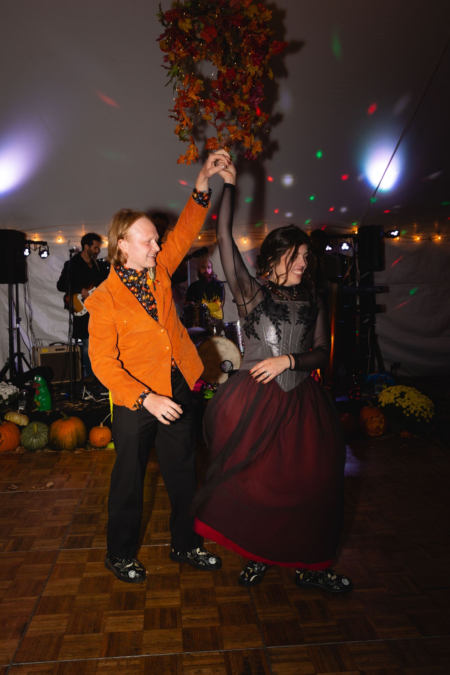 Couple dancing together at a Halloween party with orange decorations and colored disco lights illuminating the dance floor.