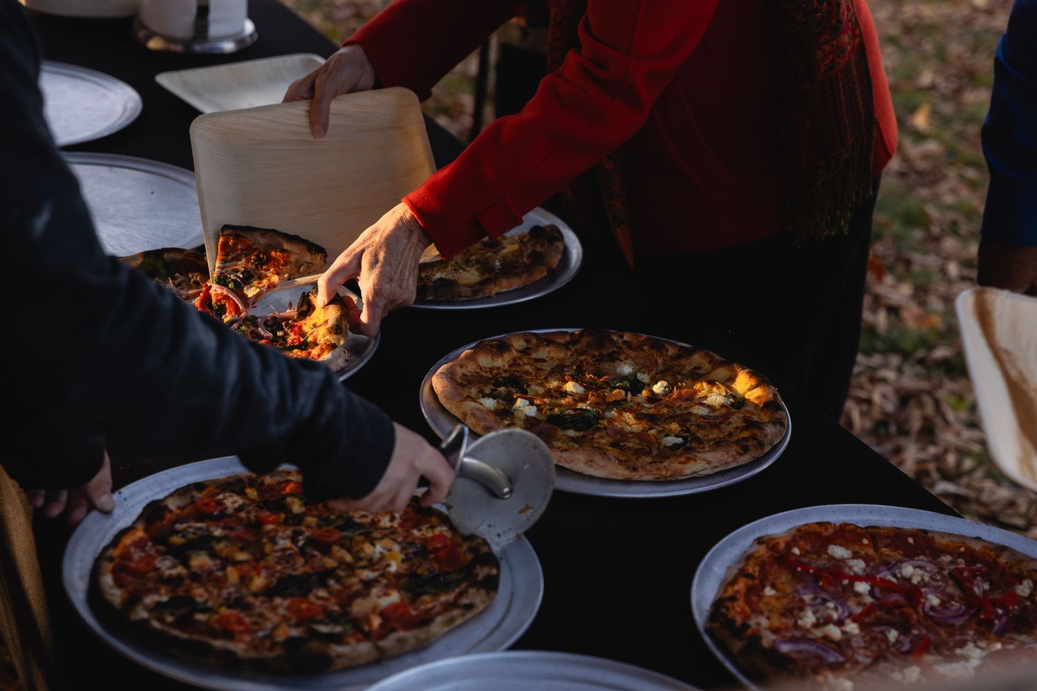 A series of wood-fired pizzas being served on rustic wooden tables with various toppings and garnishes.