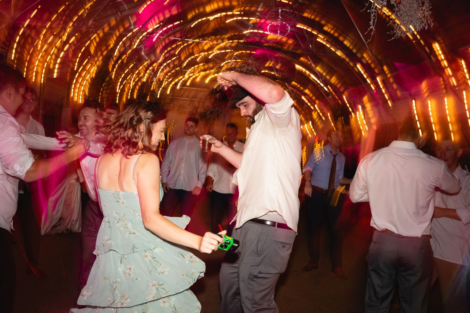 People dancing and celebrating at a wedding reception with warm ambient lighting and festive atmosphere.