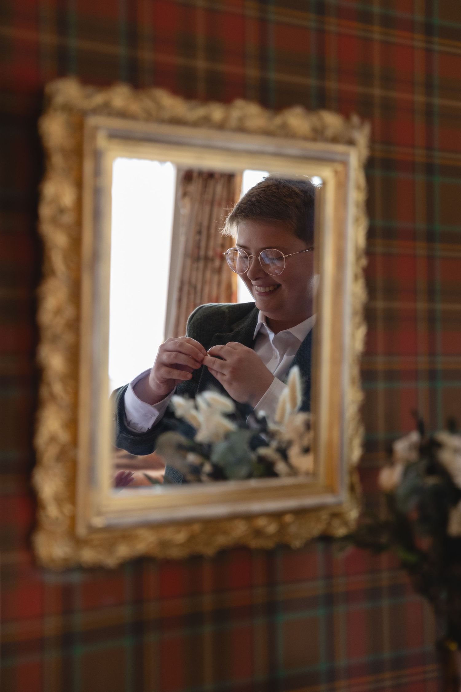 Reflection in ornate gold frame showing formal attire against plaid background.
