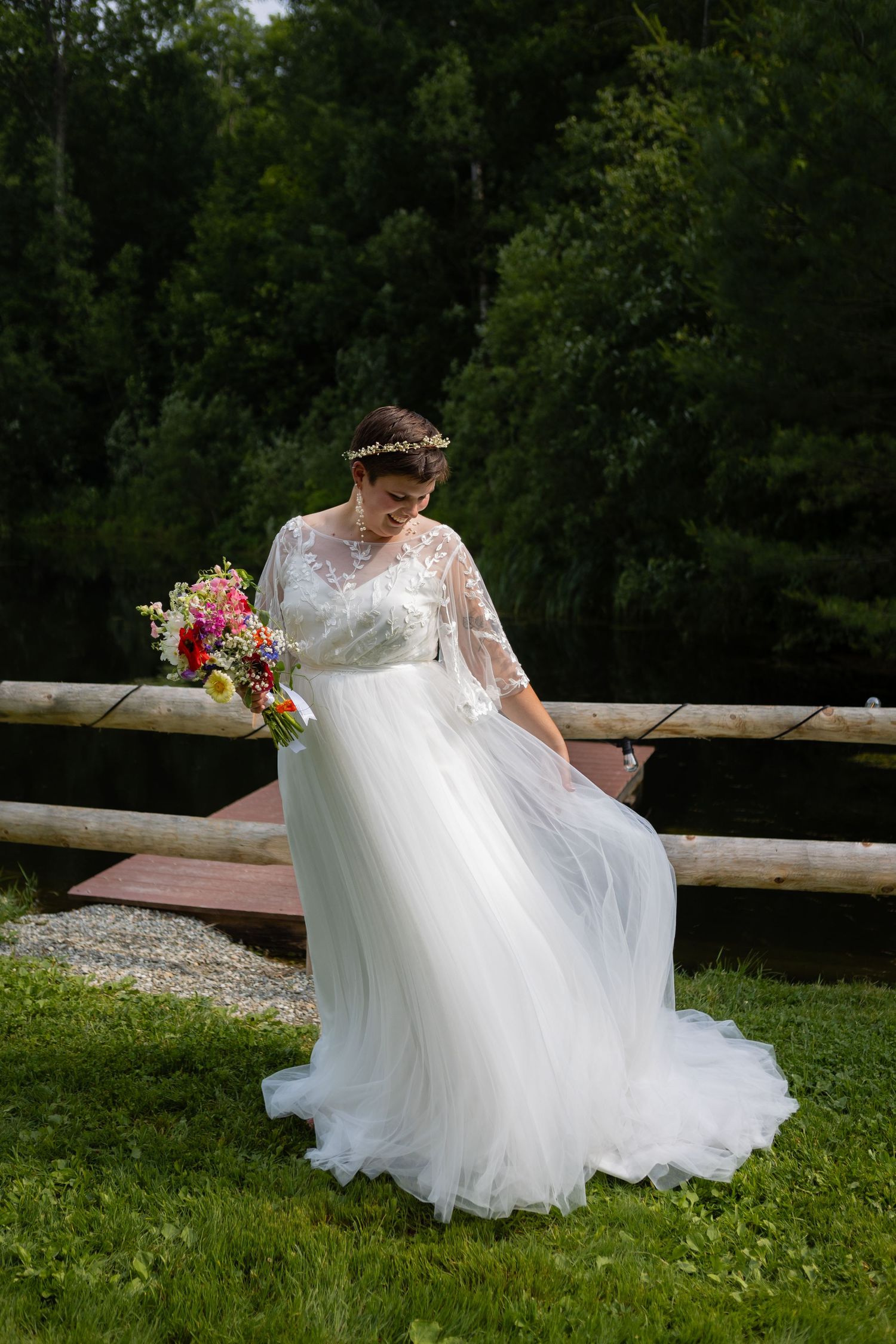 Bride in flowing white dress poses with bouquet by rustic wooden fence.