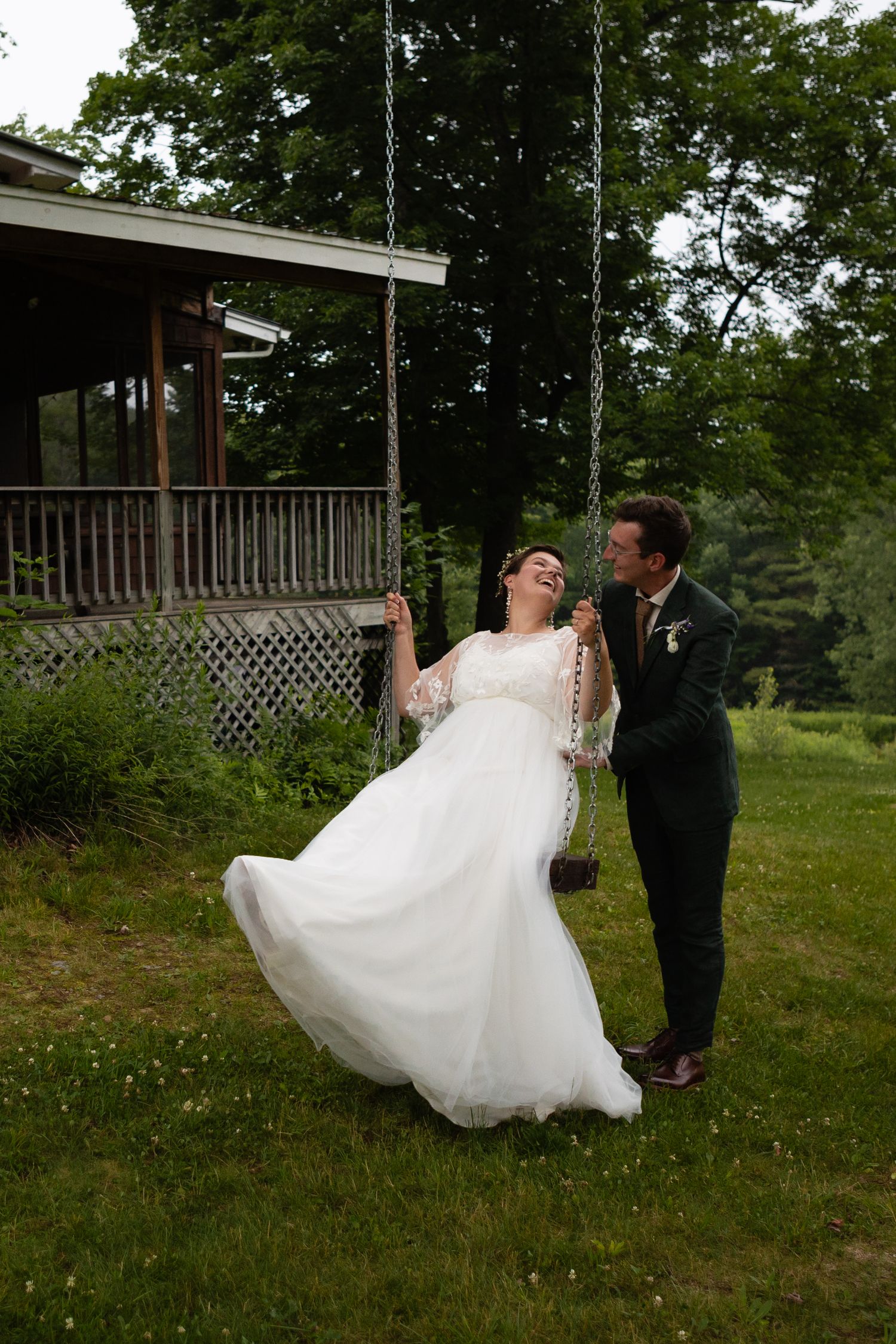 A couple plays on a swing set outside their wedding venue, with the bride's dress flowing in the breeze.