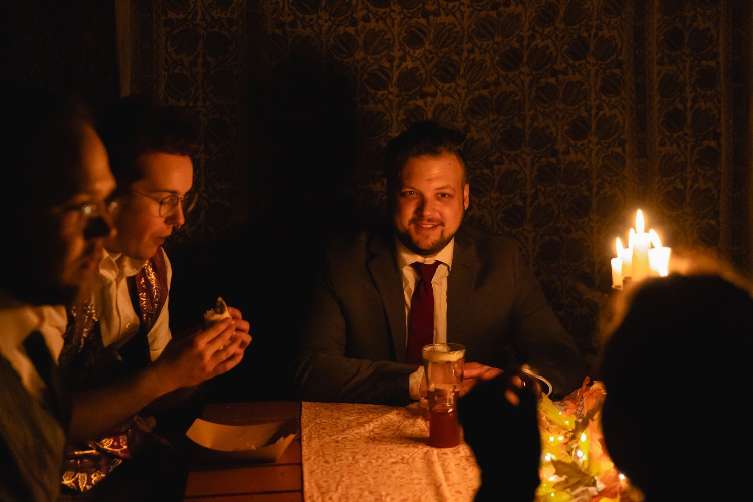 Group of guests gathered around a candlelit dinner table in a dimly lit room.