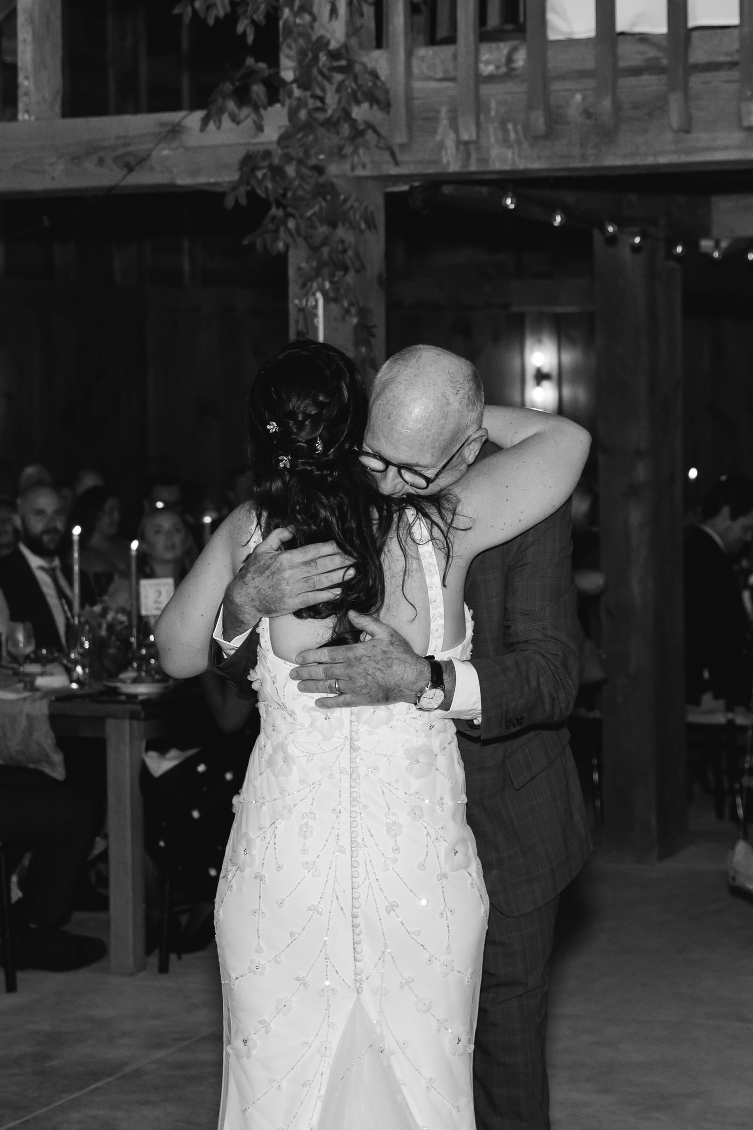 An emotional wedding dance moment between two people sharing an embrace under twinkling lights at an indoor venue.