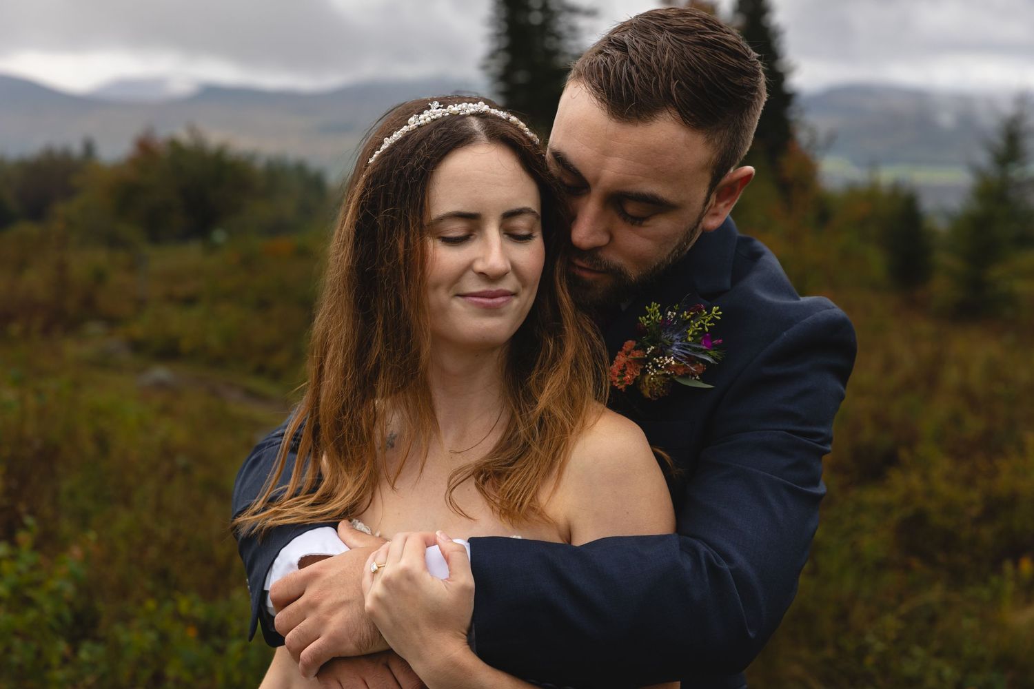 Romantic wedding couple embraces on a misty hillside with evergreen trees in the background.