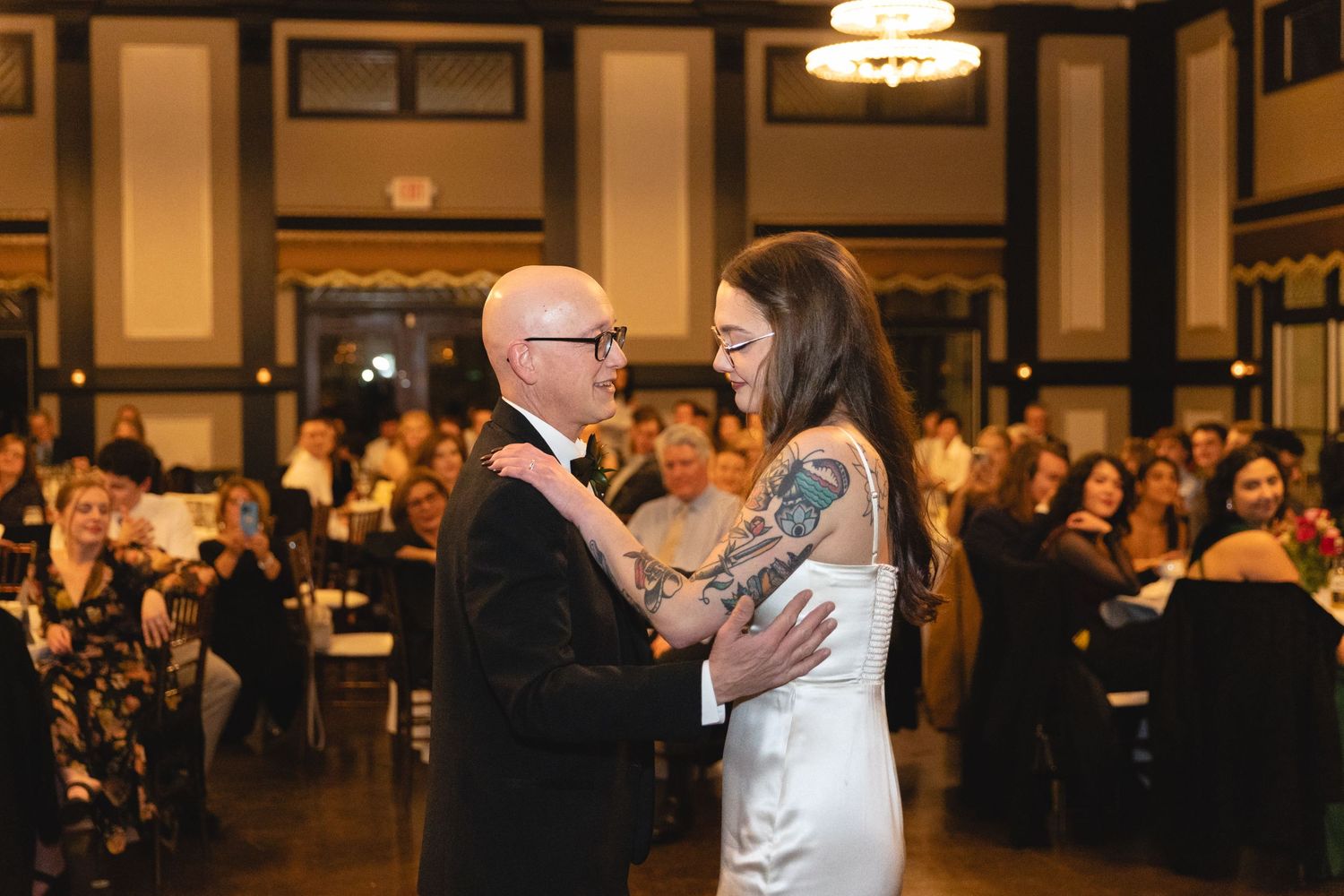 A heartwarming father-daughter dance moment at a wedding reception with guests watching in an elegant ballroom setting.