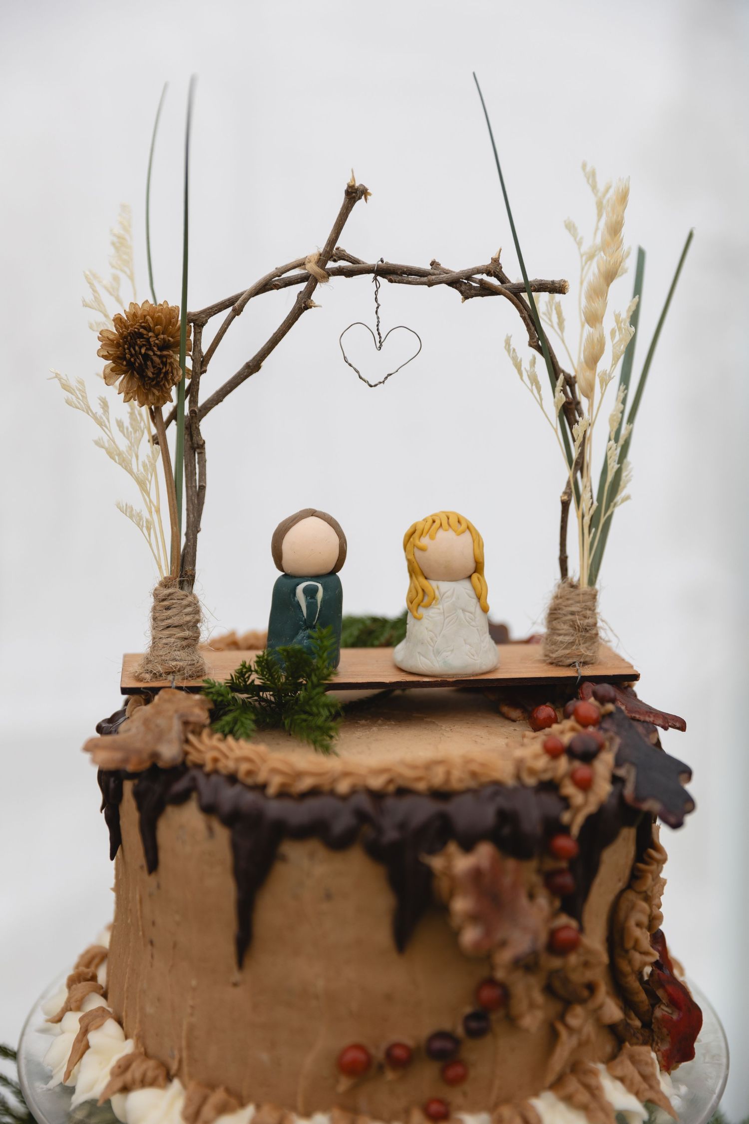 Whimsical wedding cake topper featuring handmade figurines under a twig arch.