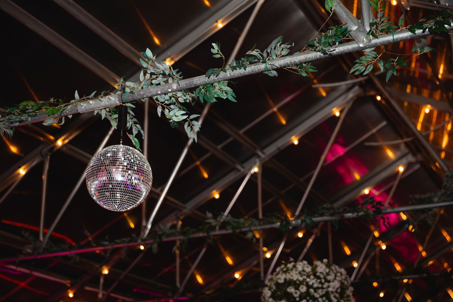 A disco ball hangs from a wooden beam decorated with greenery and twinkling lights creating a festive atmosphere.