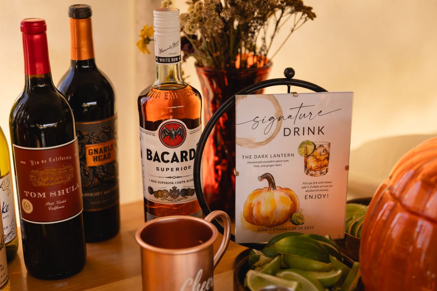 Various liquor bottles and decorative pumpkins arranged on a wooden shelf with warm lighting in the background.