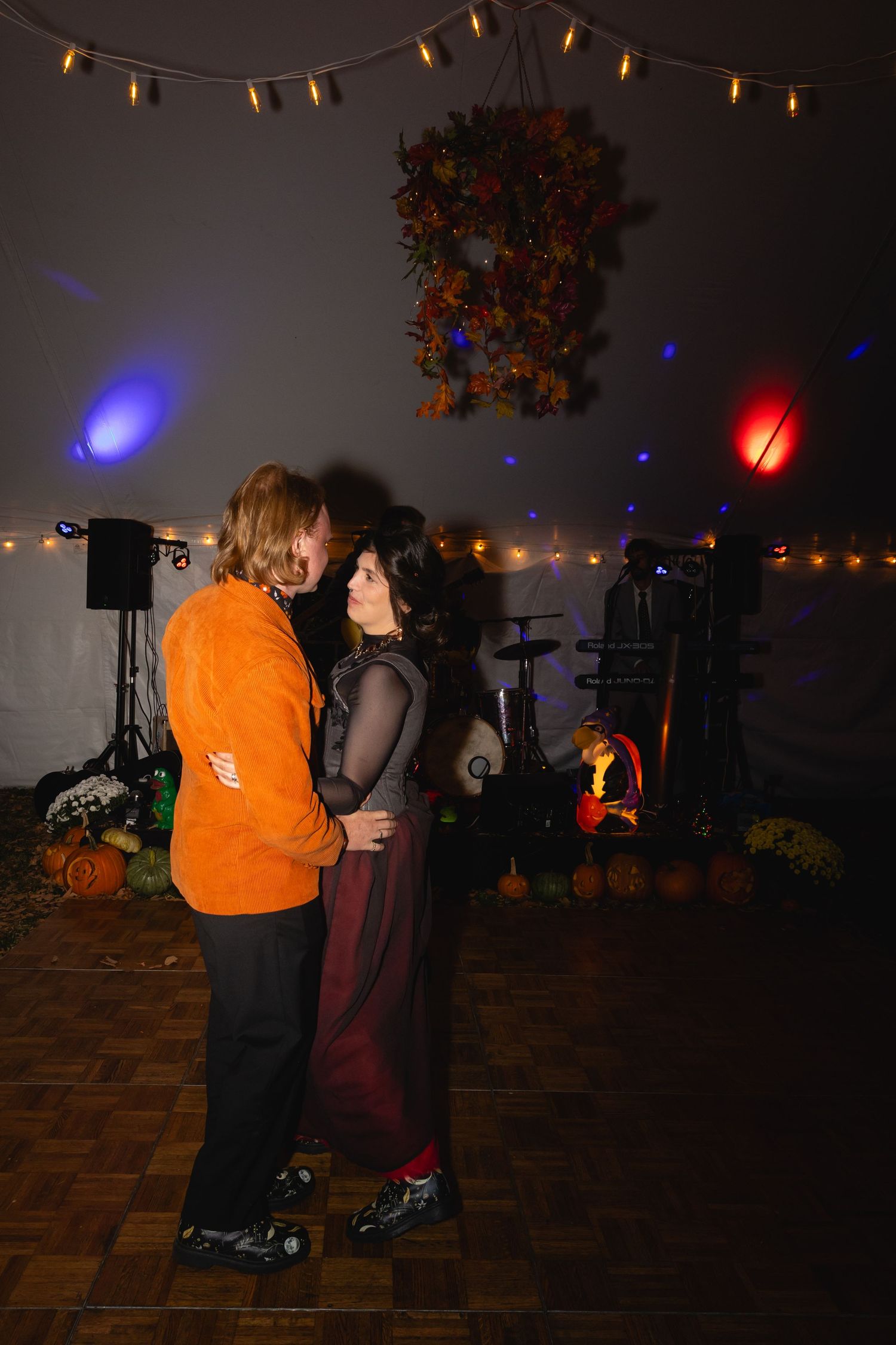 Couples slow dancing on a dimly lit dance floor decorated with string lights and fall decor for an autumn celebration.