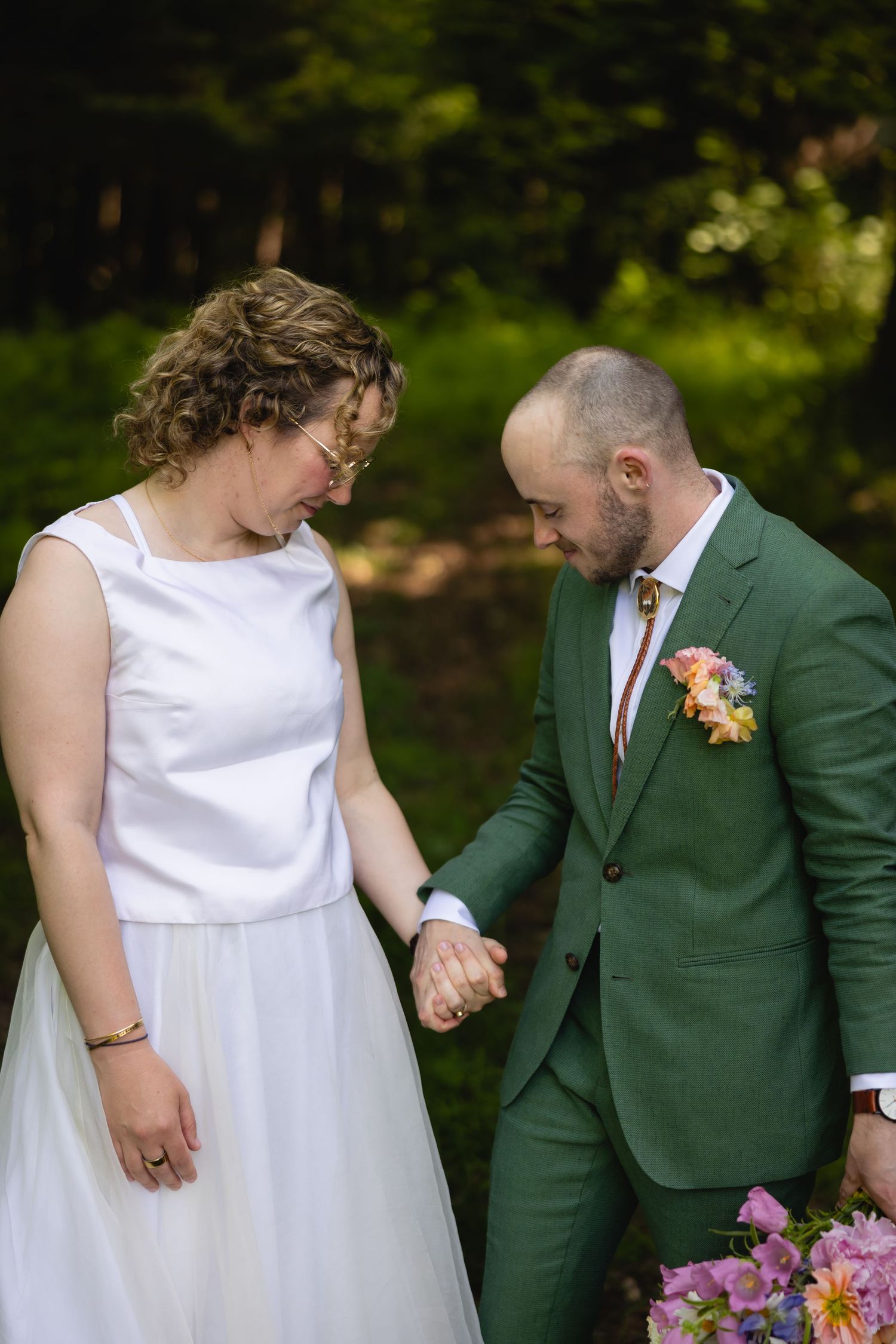 A couple in wedding attire, with a green suit and white dress, share intimate moments in an outdoor garden setting.
