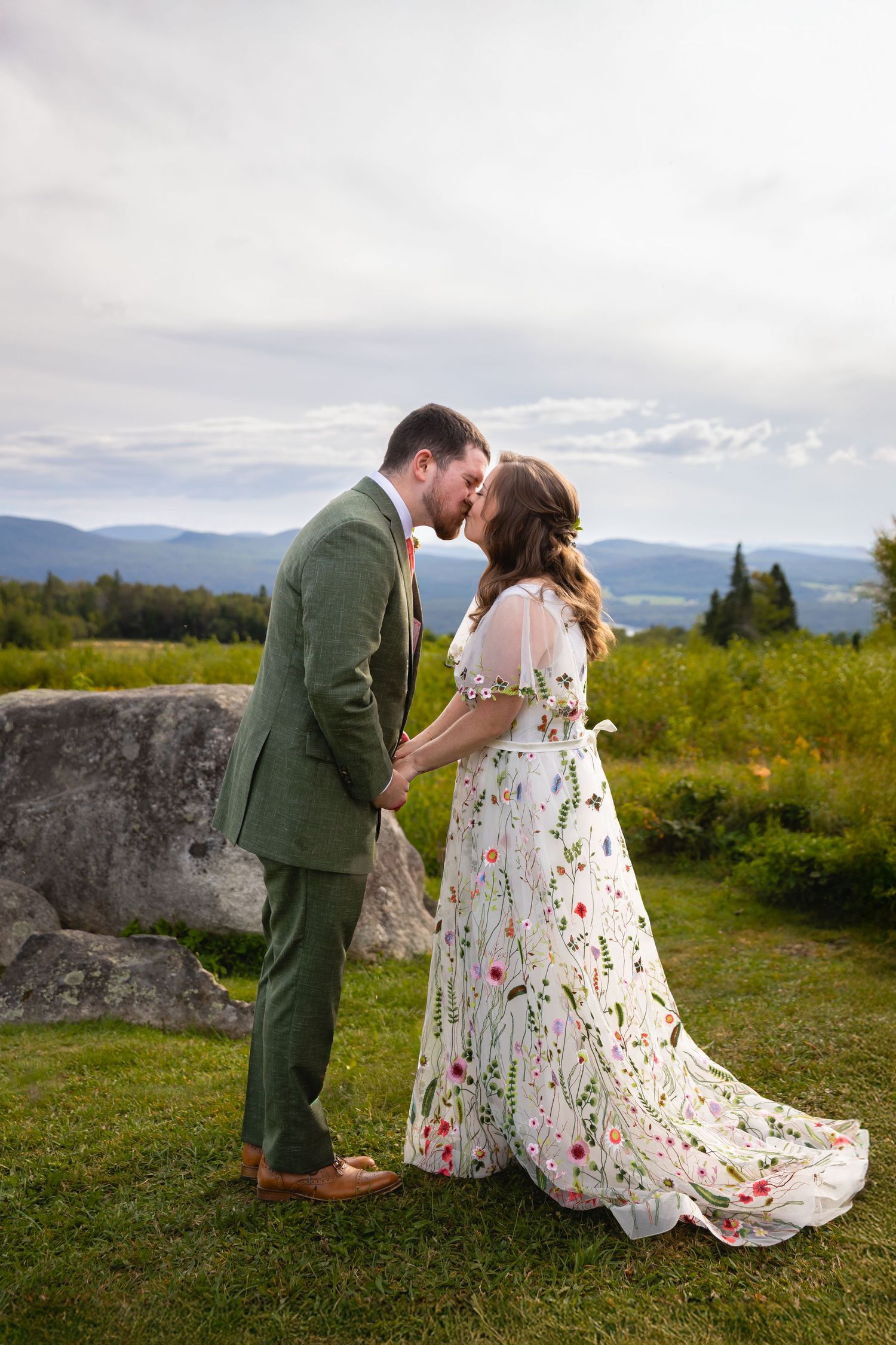 A couple shares a romantic moment on a hilltop overlooking mountains and valleys on their wedding day.