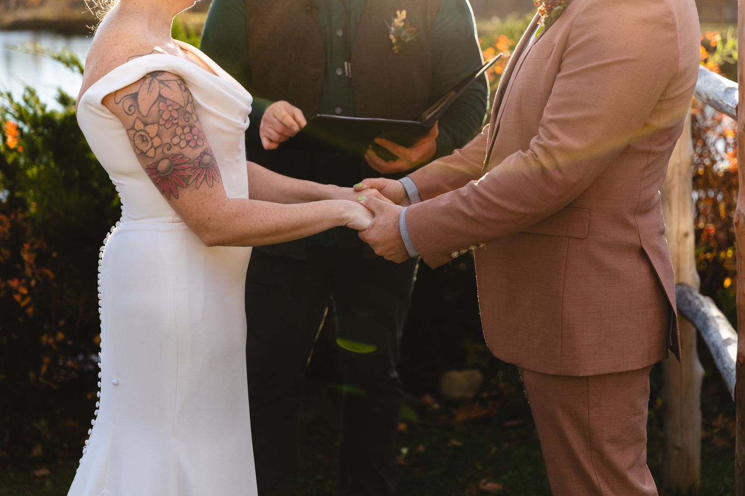 Close-up of joined hands during a wedding ceremony beneath a rustic wooden arch.
