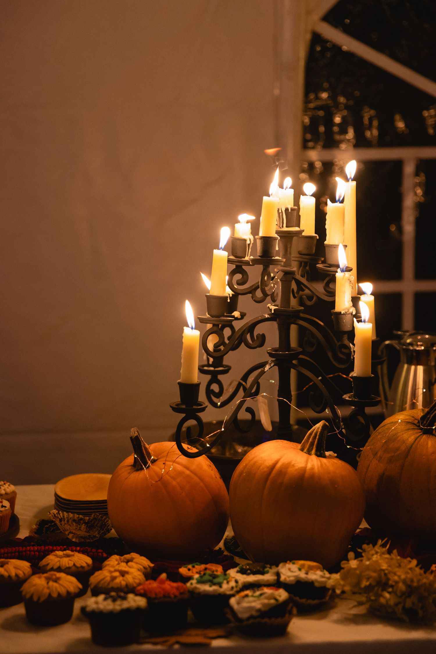 A candlelit Halloween table setting with pumpkins, cupcakes and a gothic candelabra creating a warm autumn ambiance.