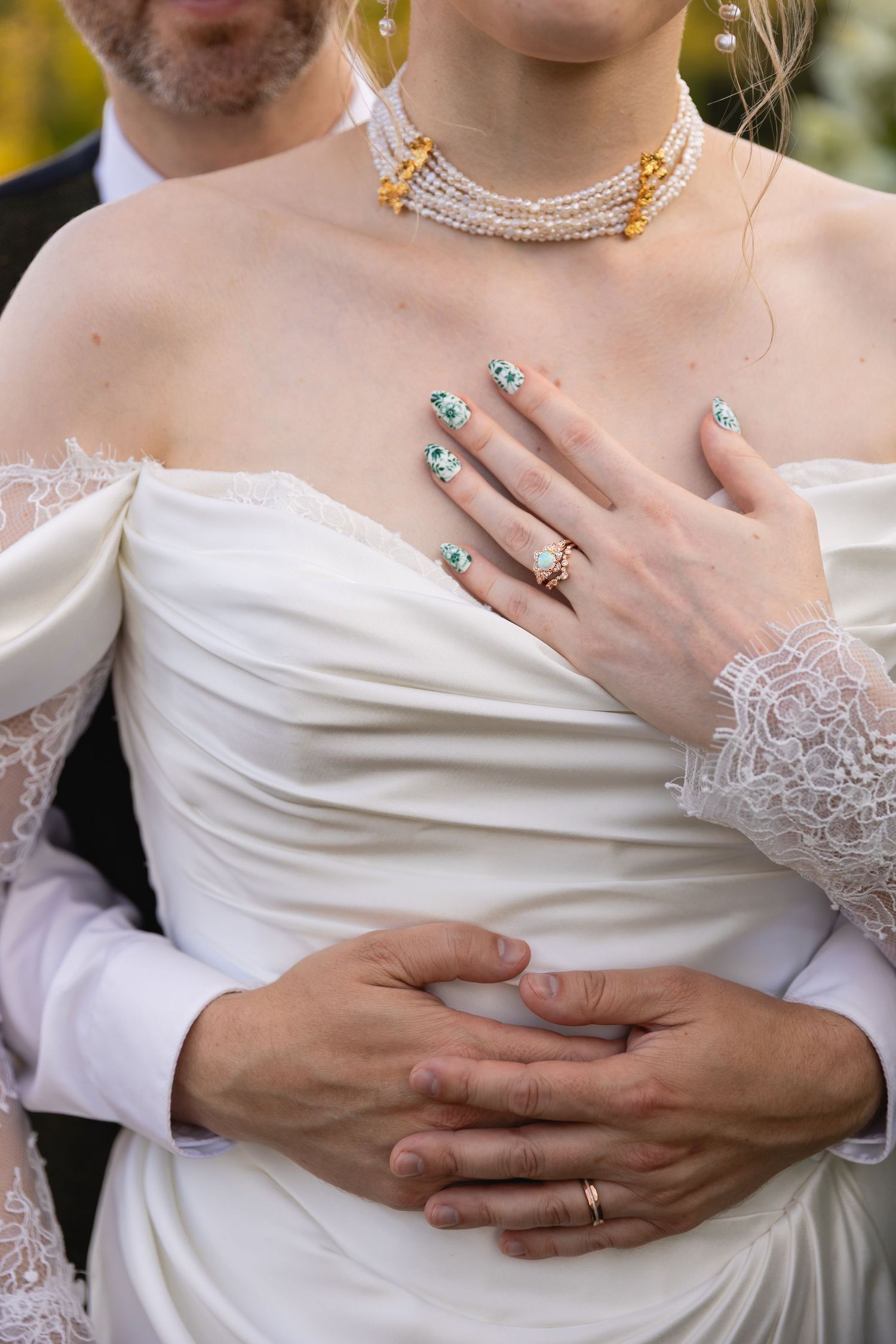 Close-up shots of hands wearing wedding rings embracing against white bridal gown with delicate lace details.