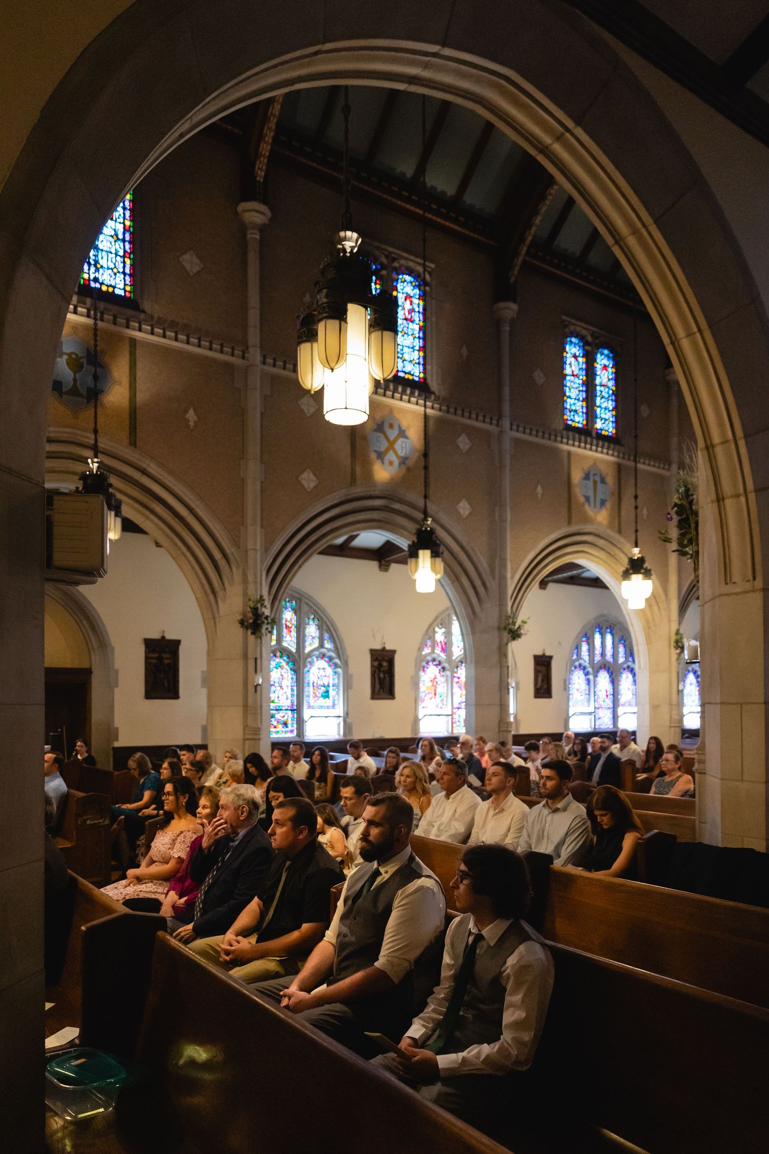 A panoramic view of people seated in wooden pews inside a historic church with arched ceilings and stained glass windows.