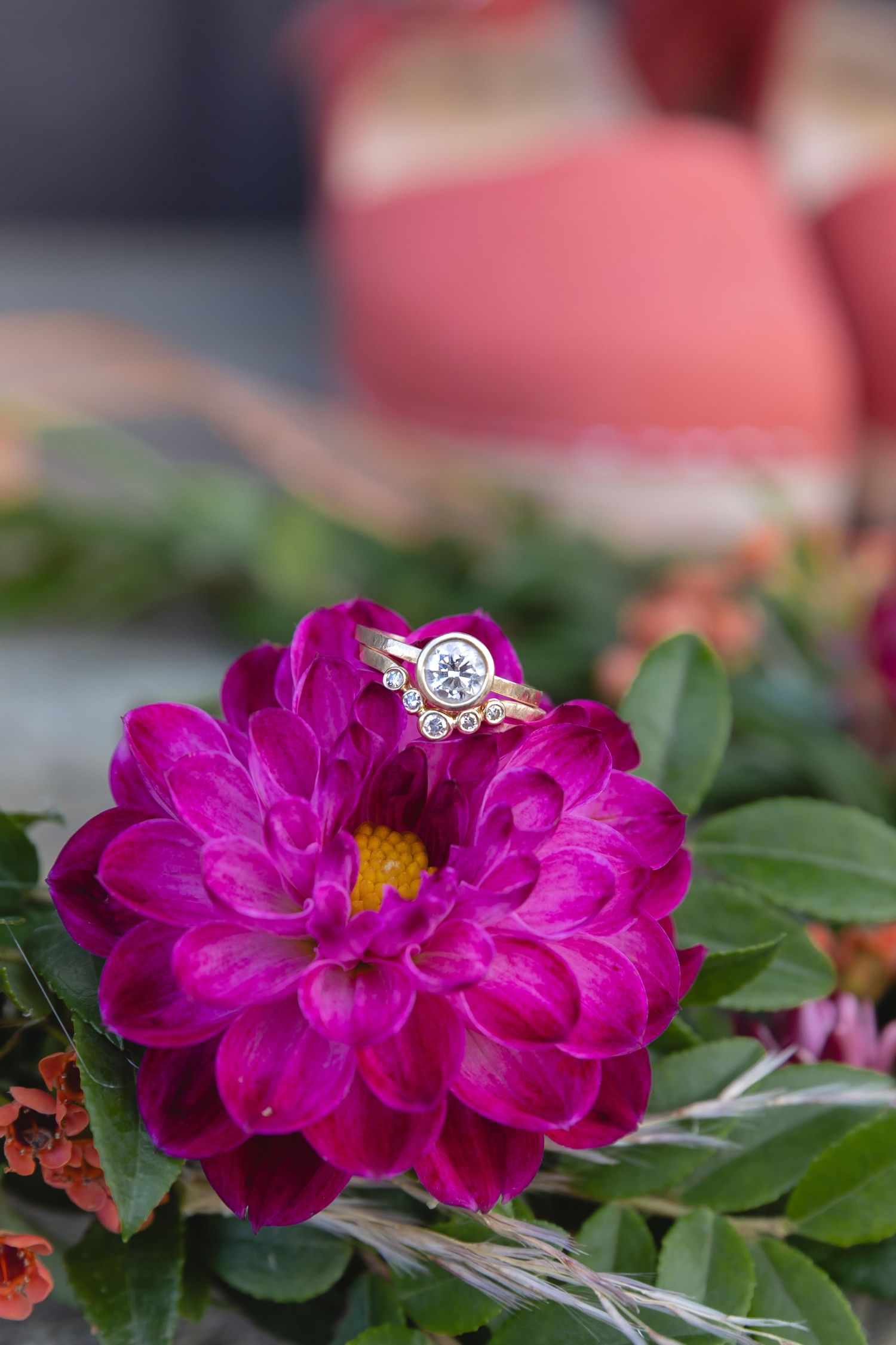 Diamond engagement ring nestled on vibrant pink dahlia flower with green leaves.