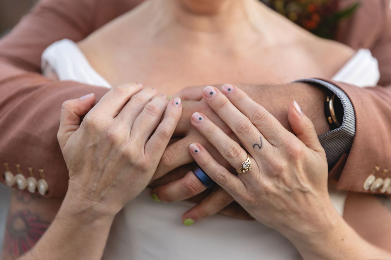 Close-up of newlywed couple's hands with rings and delicate nail art.