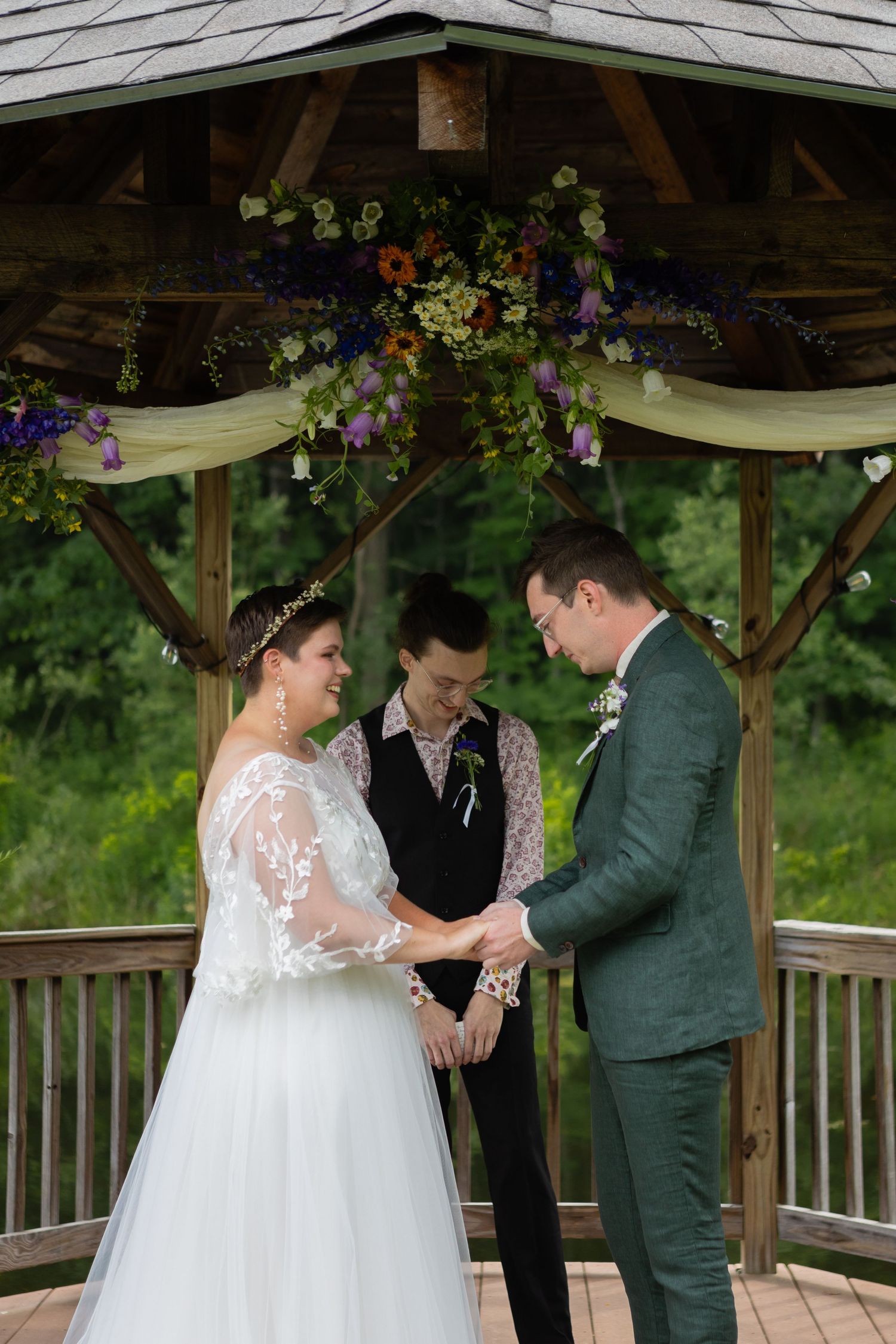 Wedding ceremony taking place in a wooden gazebo decorated with colorful floral arrangements and cream fabric draping.