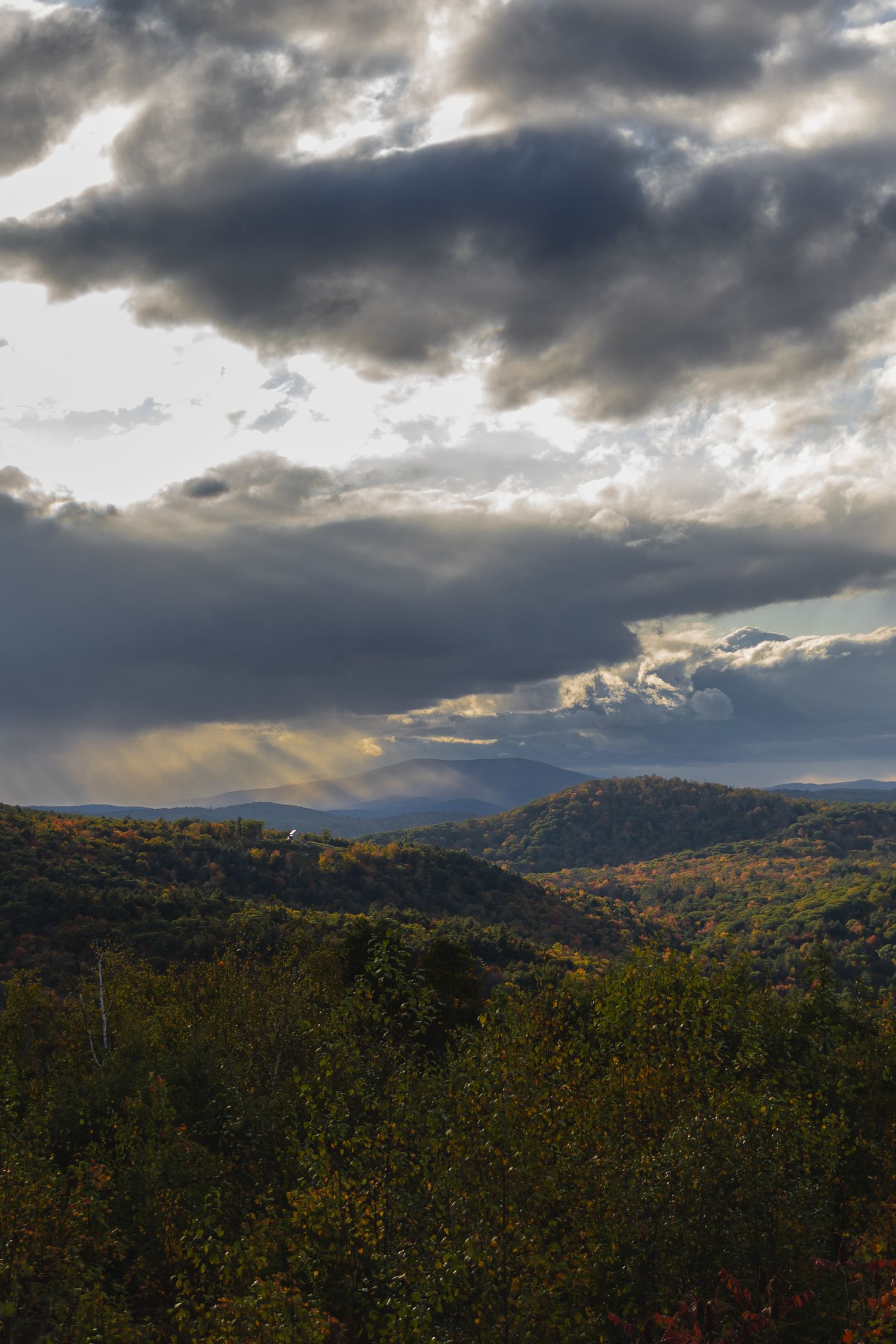 Dramatic storm clouds roll over autumn-colored mountains during sunset.