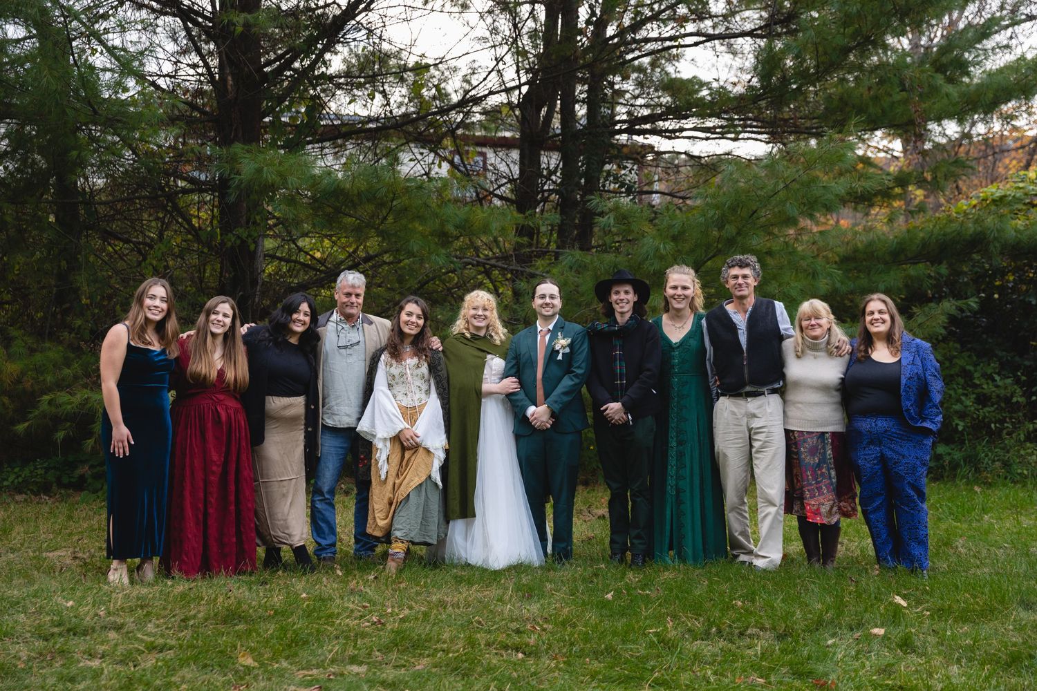 Wedding party poses together outdoors wearing mix of formal attire in autumn setting.