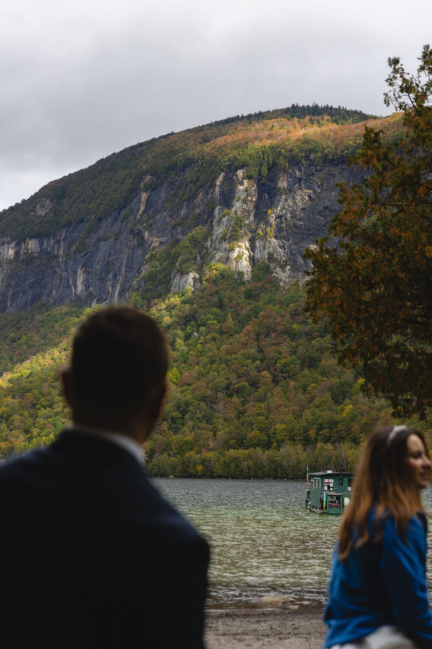 Scenic mountain cliffs rise above a lake with autumn trees in the foreground.