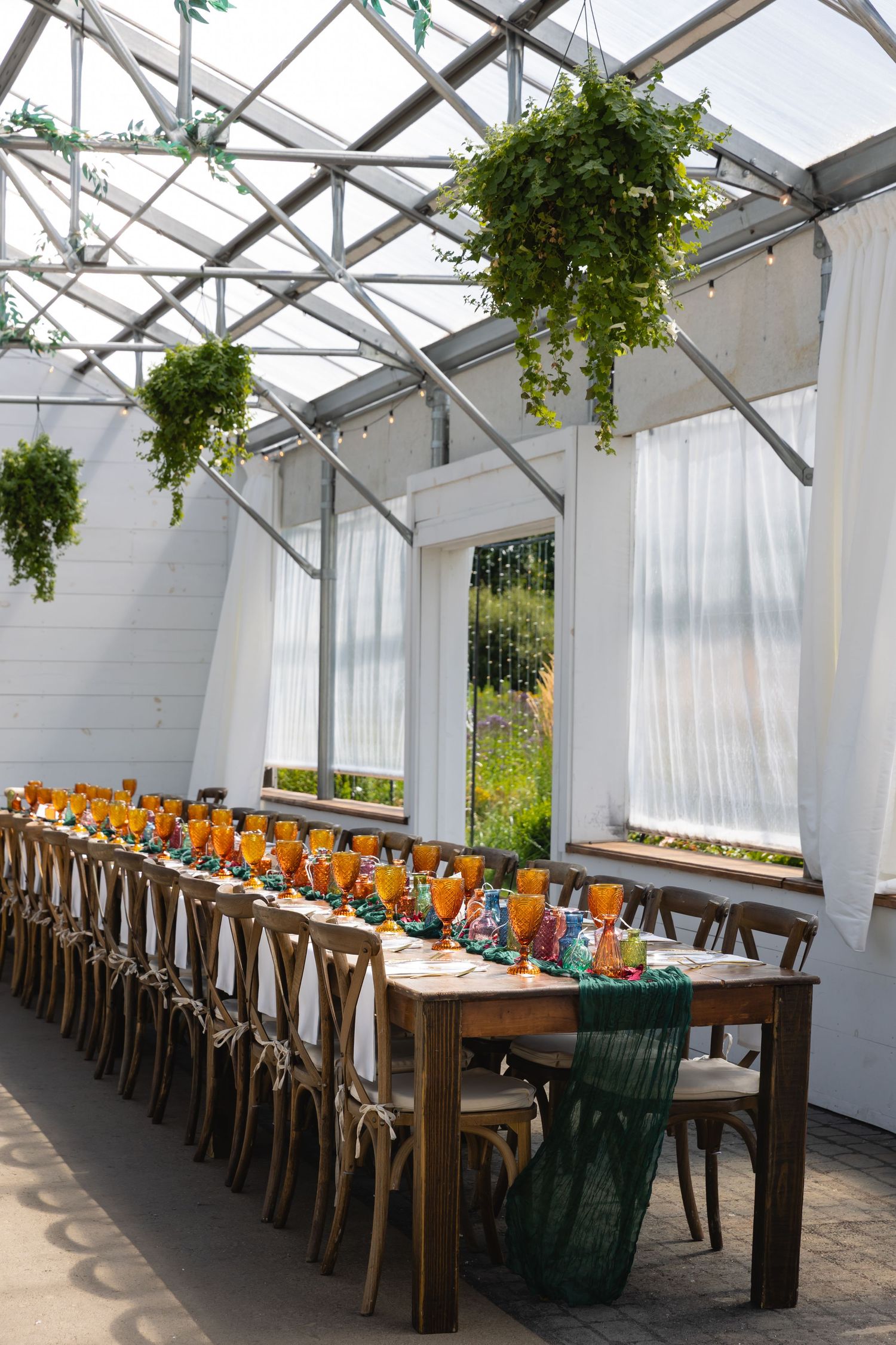 Elegant greenhouse wedding reception with long wooden tables and hanging greenery.