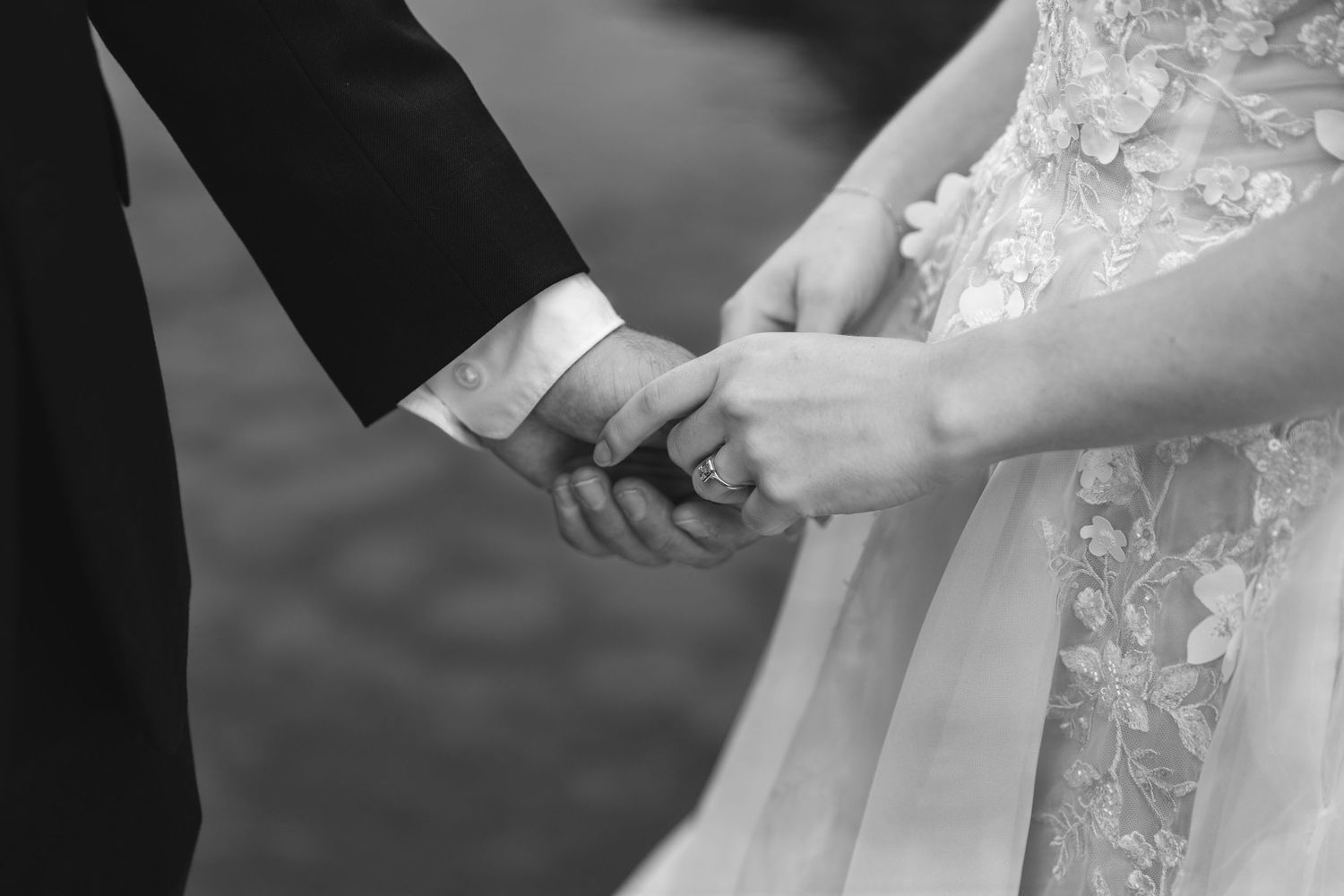 Black and white detail shot of newlyweds holding hands showing wedding attire.