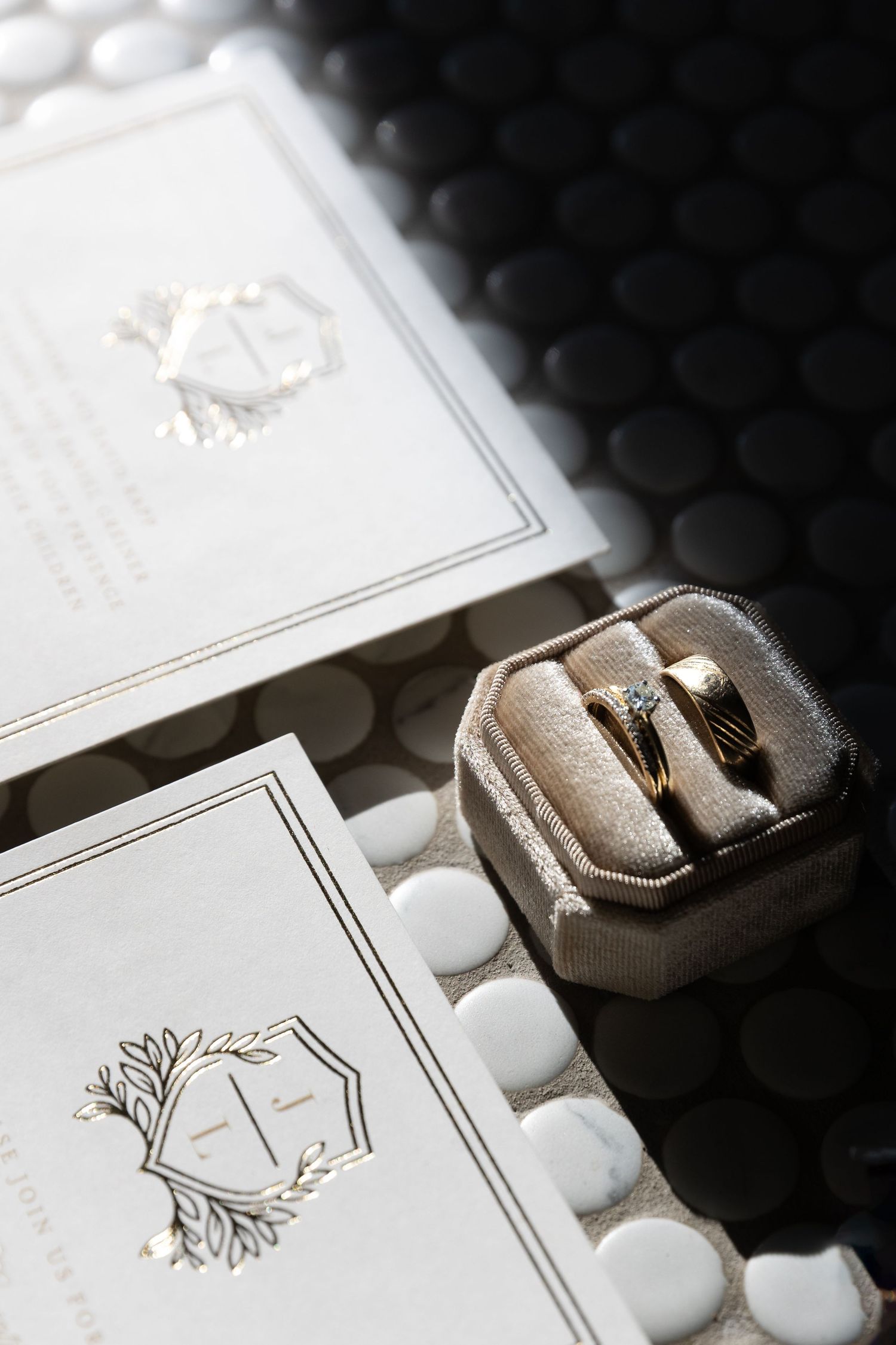 Two elegant wedding rings rest in a grey velvet box beside white stationery with a monogram design and decorative details.