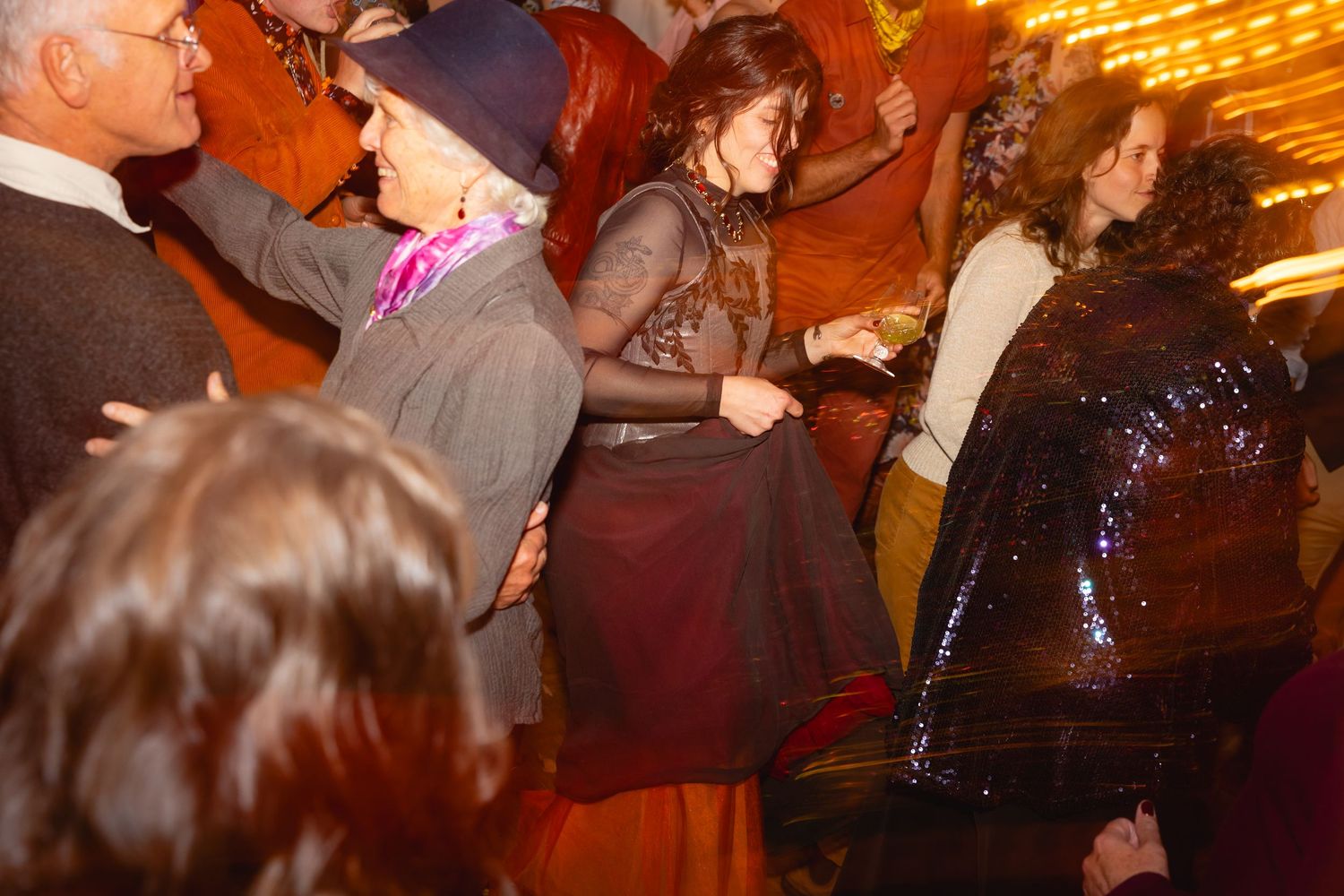 People dancing and socializing at a dimly lit party venue with warm amber lighting and festive atmosphere.