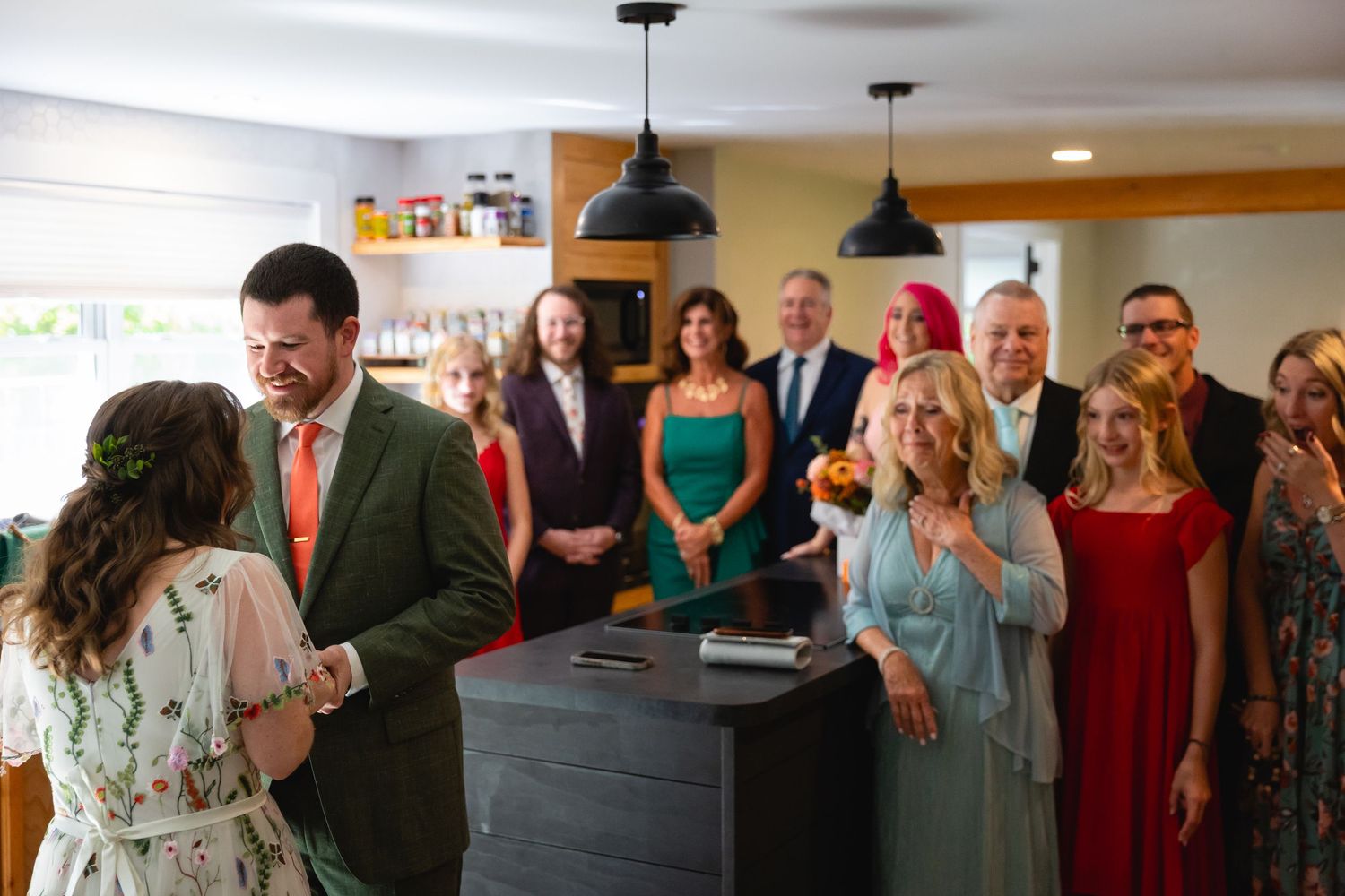 Wedding guests gather in an indoor venue space during a celebration with pendant lighting and warm decor.