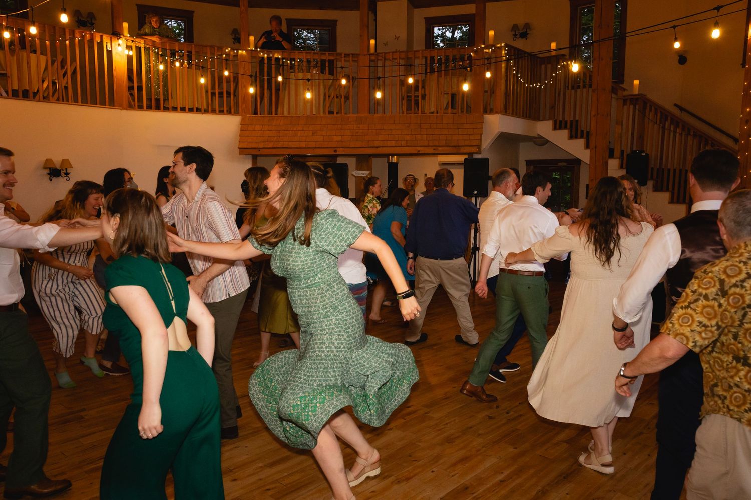 People dance together in pairs during a traditional folk dance event in a warmly lit community hall.